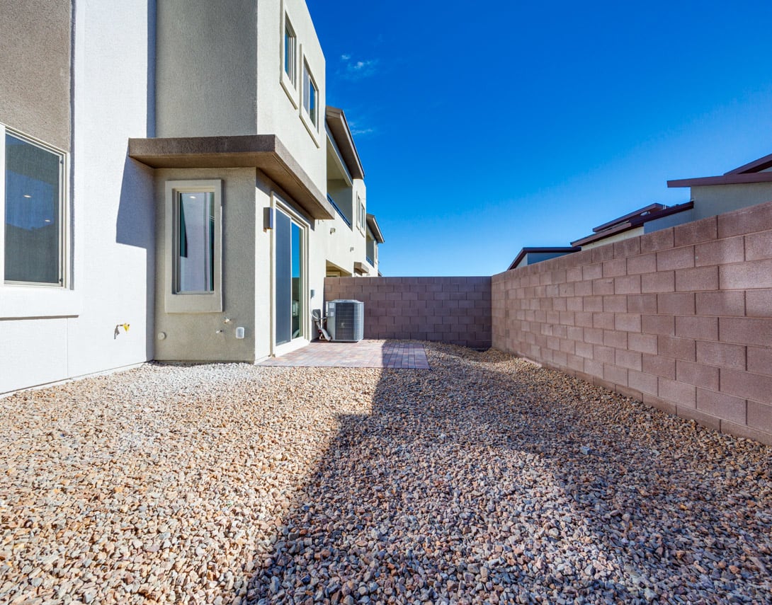 A modern residential building with a gravel-covered pathway leading to the entrance, set against a clear blue sky.
