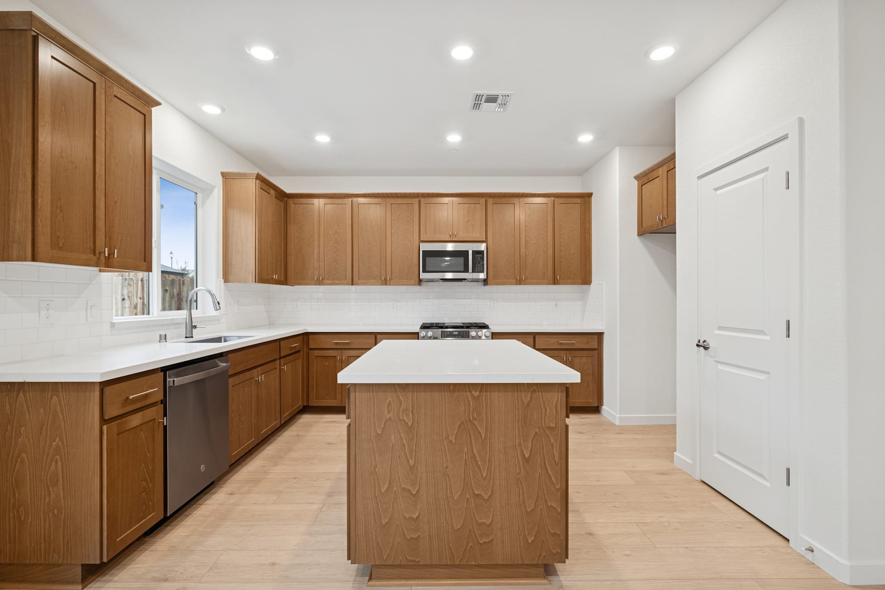 A modern, well-lit kitchen with wooden cabinets, a white countertop, and stainless steel appliances.