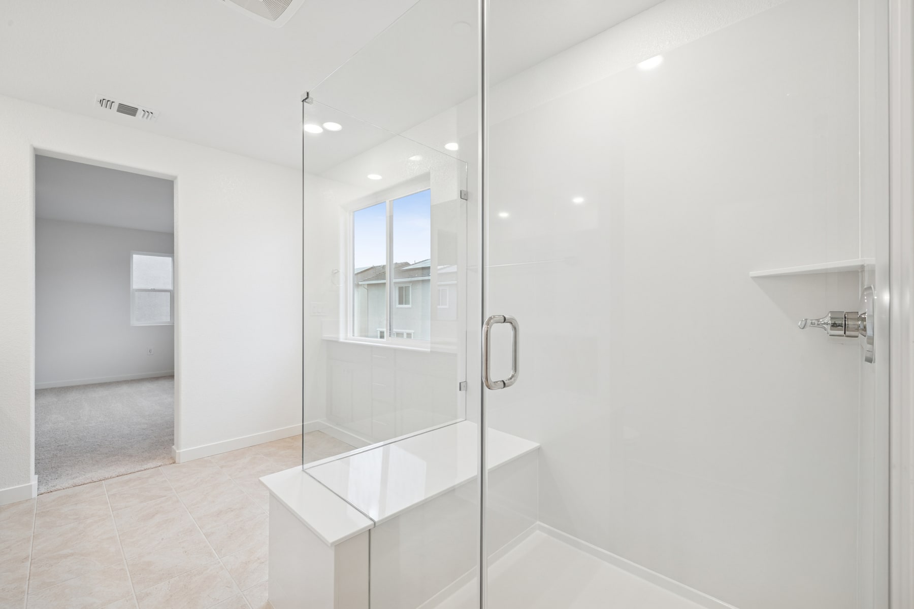 A bright, modern bathroom with a glass shower enclosure, white walls, and recessed lighting.