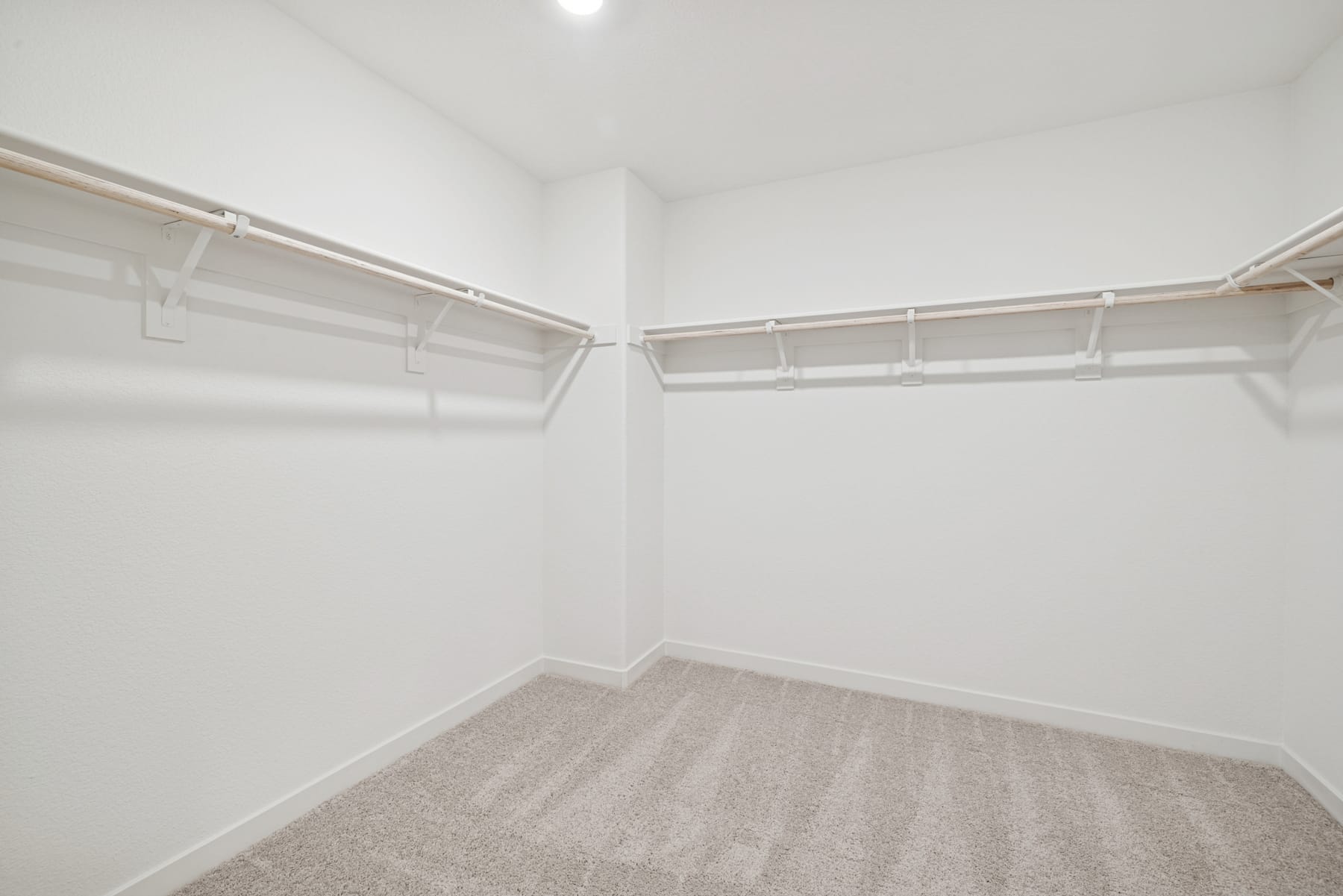 A spacious, well-lit walk-in closet with white walls, a carpeted floor, and a series of shelves and hanging rods for storage.