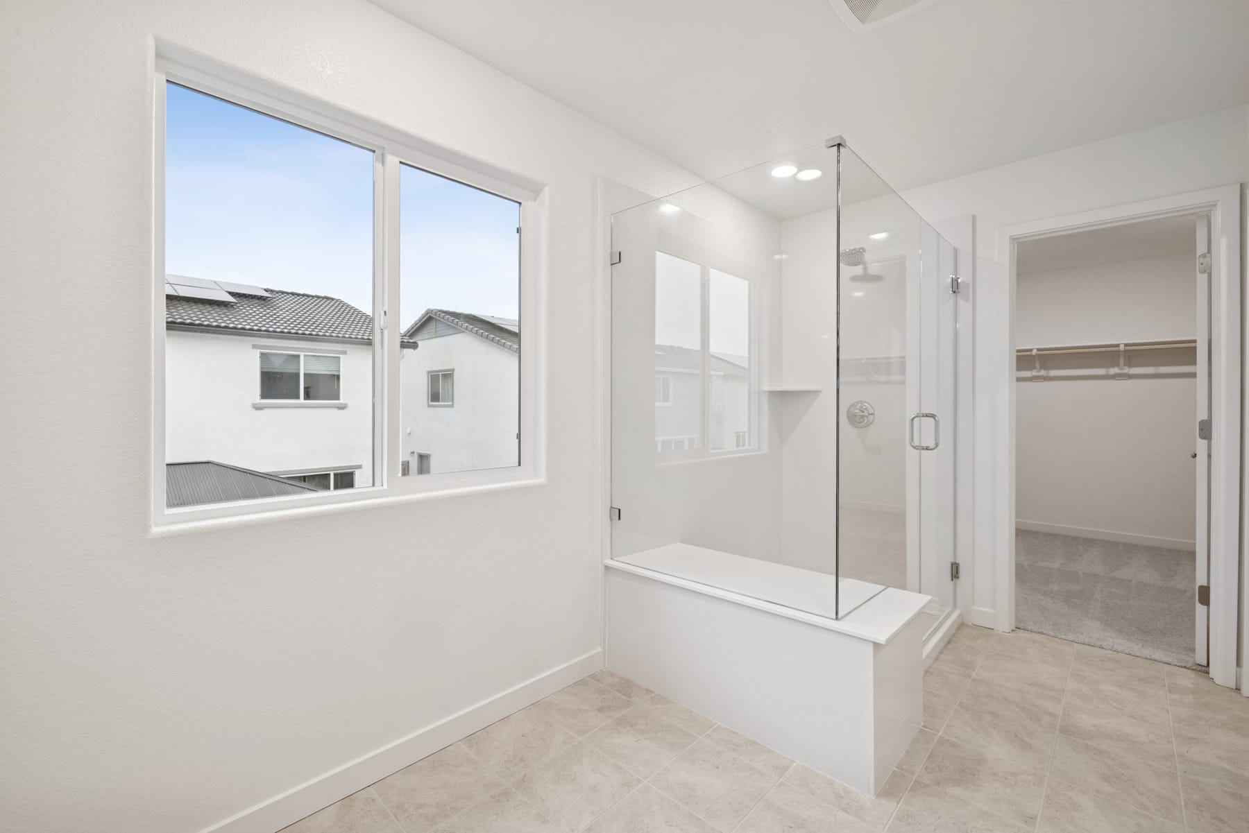 A bright and spacious bathroom with a large window, a glass shower enclosure, and a tiled floor.