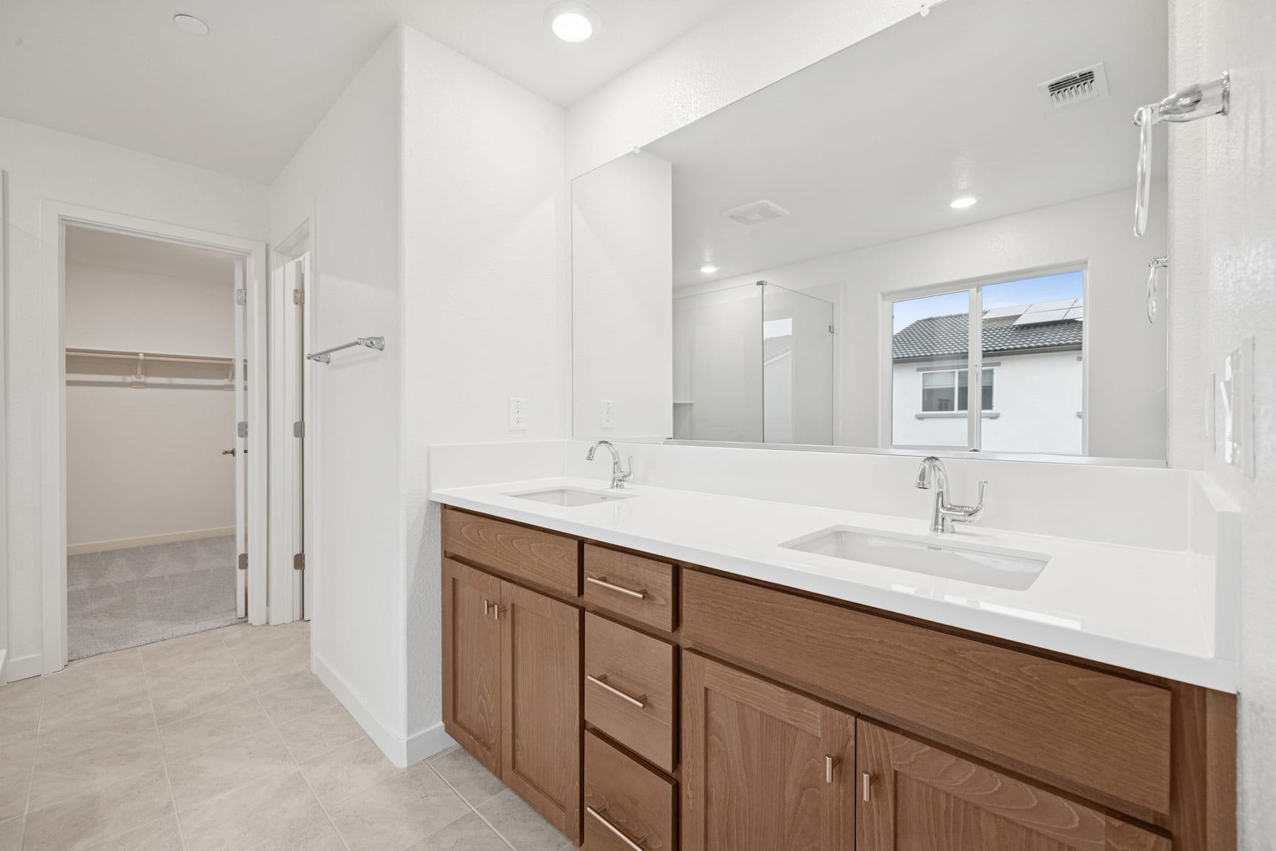 A modern and spacious bathroom with a large vanity, double sinks, and a mirror taking up the entire wall, set against a bright and airy backdrop.