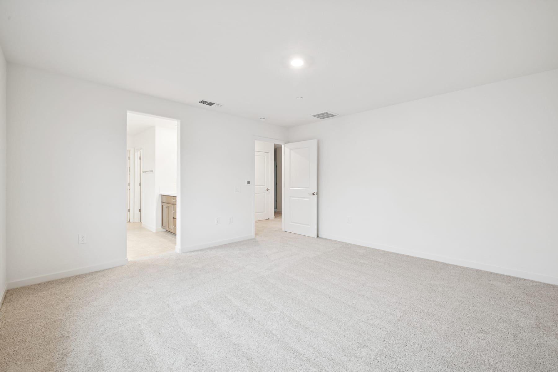A spacious, minimalist room with white walls, a light-colored hardwood floor, and a recessed ceiling light.