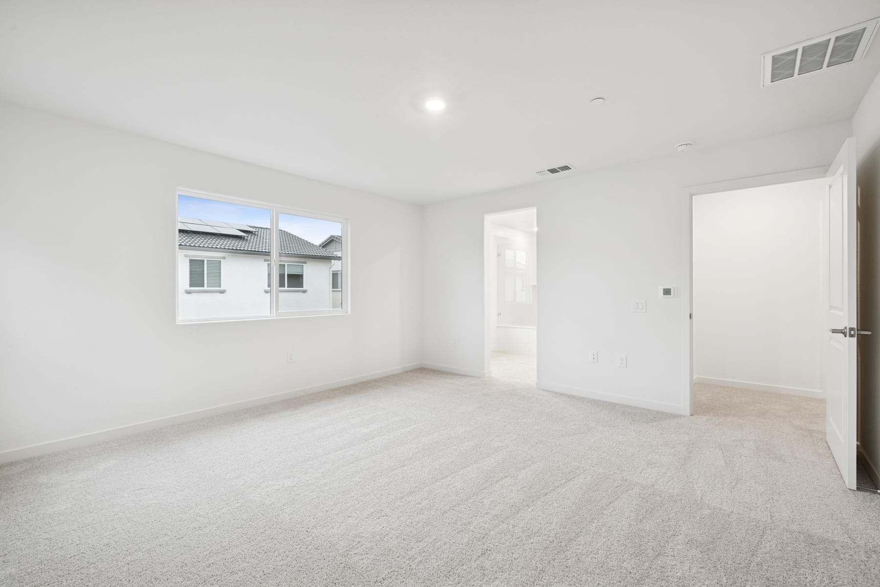 A spacious, bright, and minimalist room with white walls, a carpeted floor, and a window providing natural light.