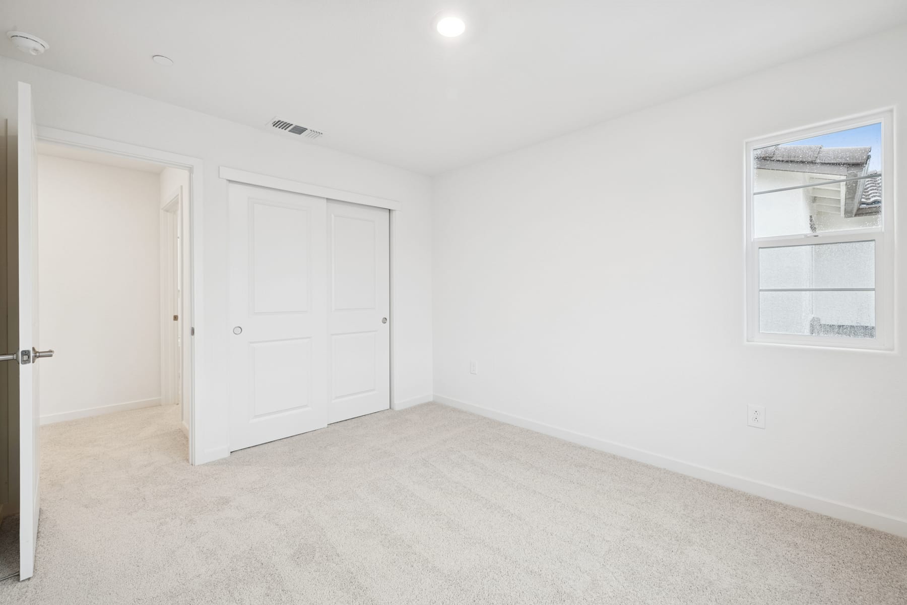 A bright, spacious room with white walls, a carpeted floor, and a closed door leading to another room.
