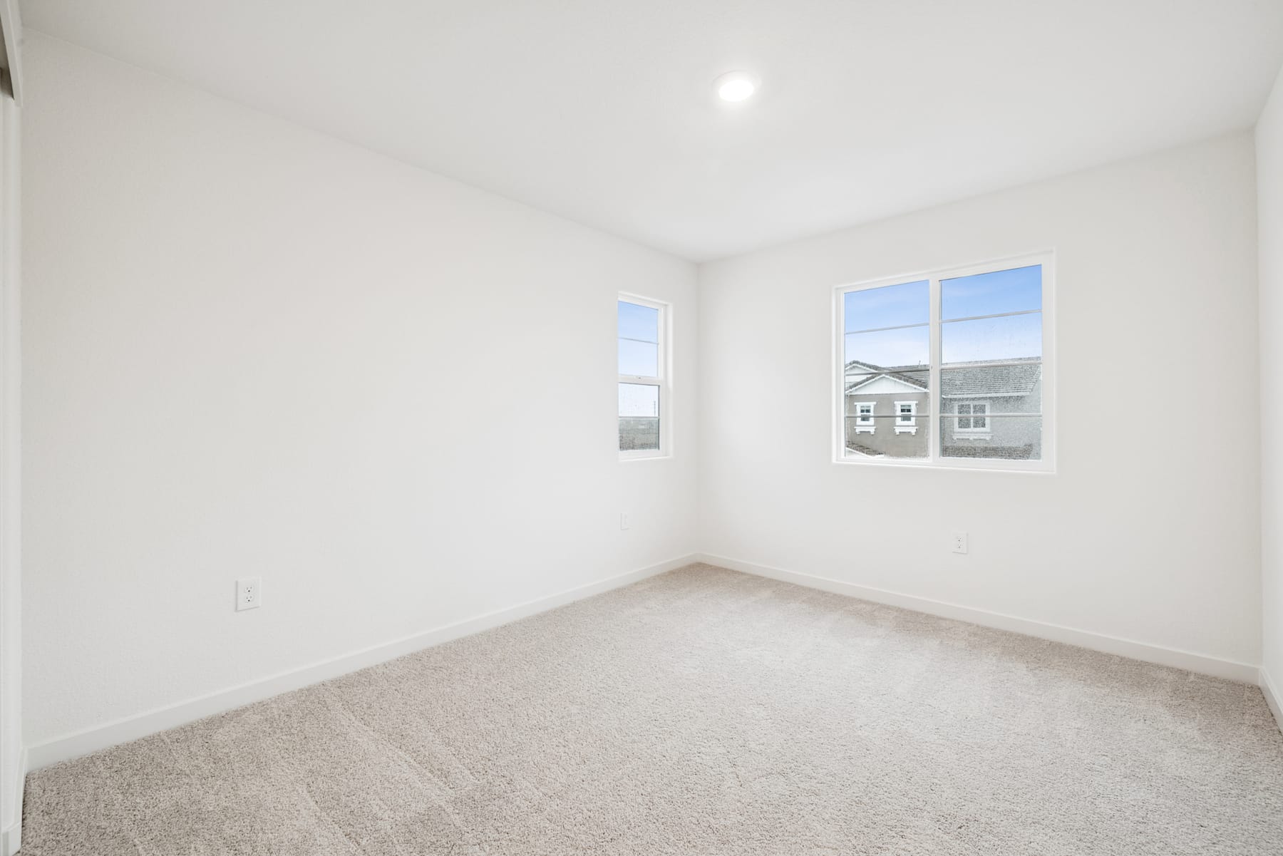 A bright, empty room with white walls, a carpeted floor, and two windows providing natural light.