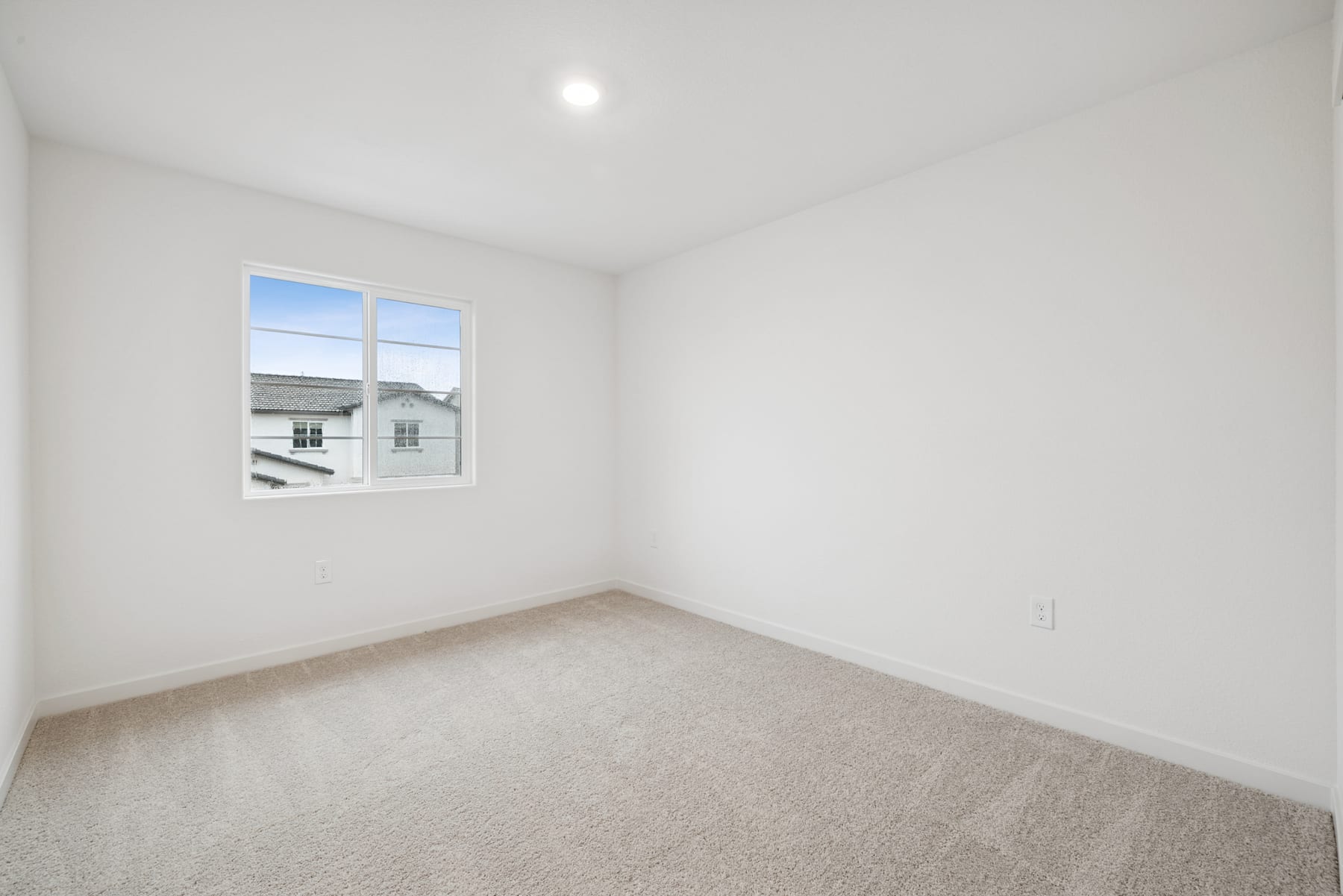A bright, empty room with a window overlooking a residential neighborhood in the background.