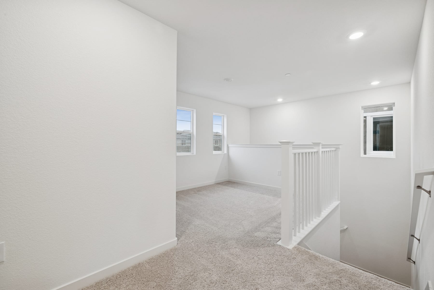 A bright, open hallway with white walls, a carpeted floor, and a railing leading to a second level.