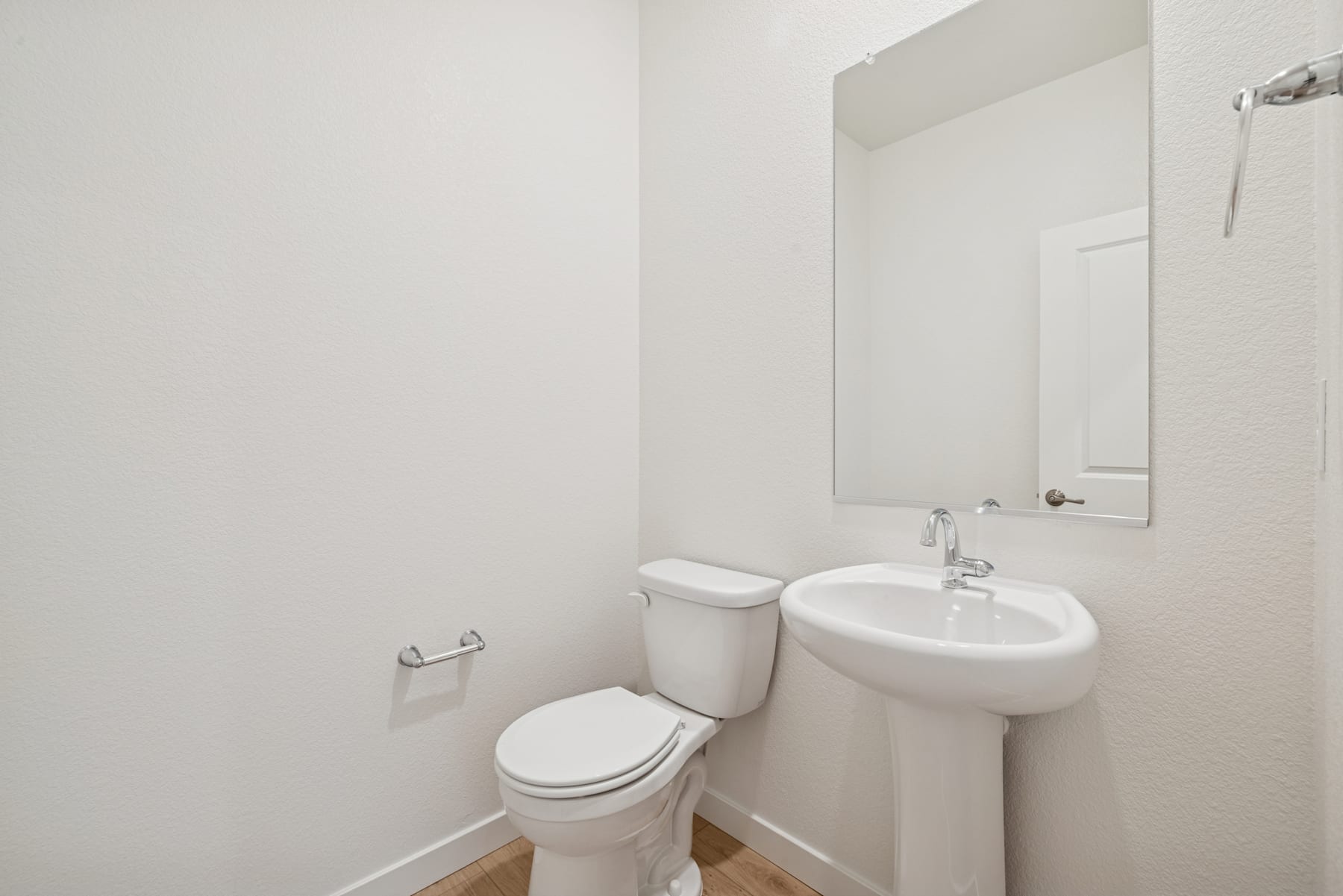 A simple and clean bathroom interior with a toilet, sink, and mirror on the wall.