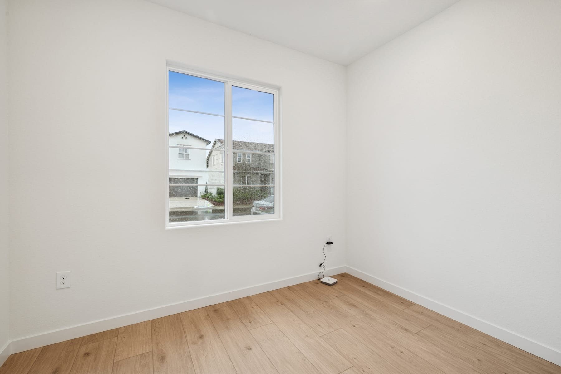 A bright, empty room with a large window overlooking a residential neighborhood in the background.