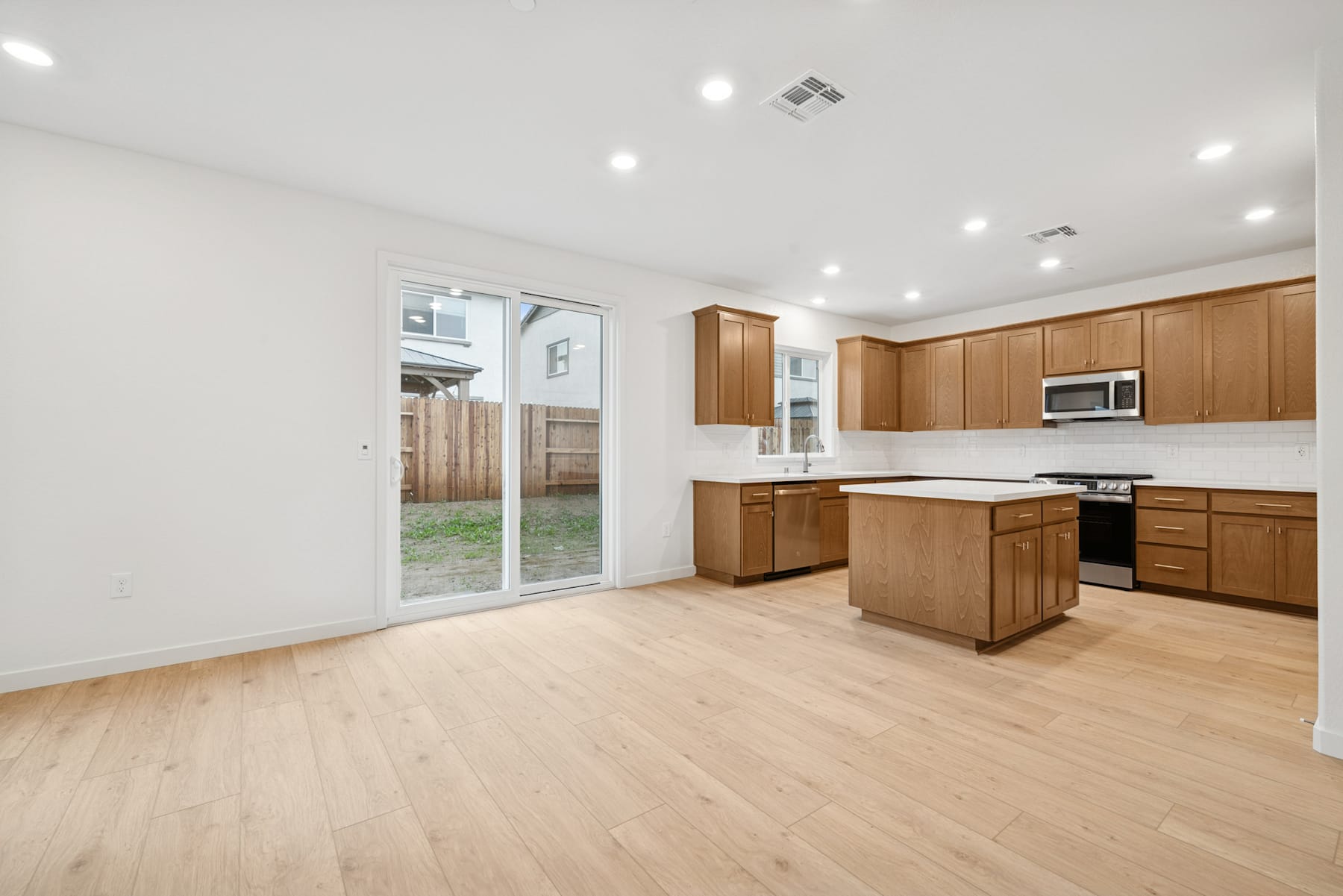 A spacious and modern kitchen with wooden cabinets, a white countertop, and a sliding glass door leading to the backyard.