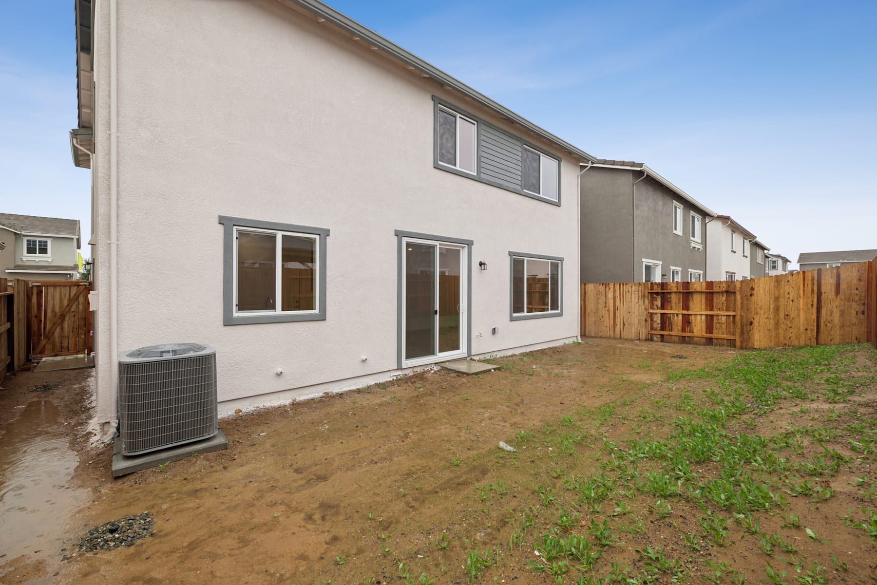 A two-story residential building with a grassy yard and a wooden fence in the foreground, set against a clear blue sky.