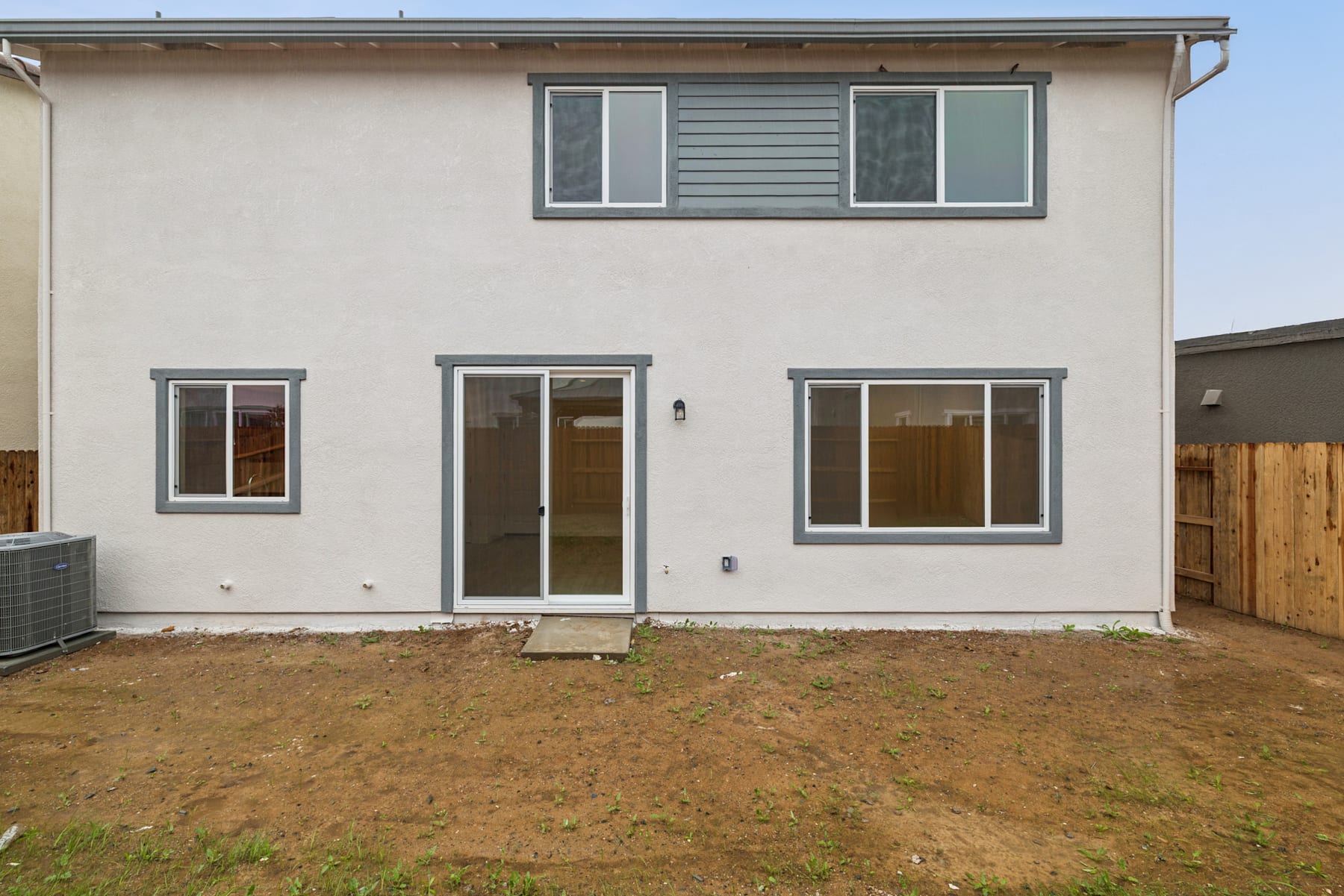 A two-story residential building with a grassy yard in the foreground and a wooden fence in the background.