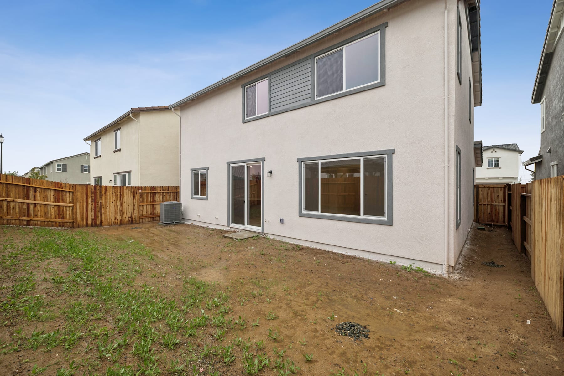 A two-story residential building with a wooden fence in the foreground, surrounded by a grassy yard and set against a clear blue sky.