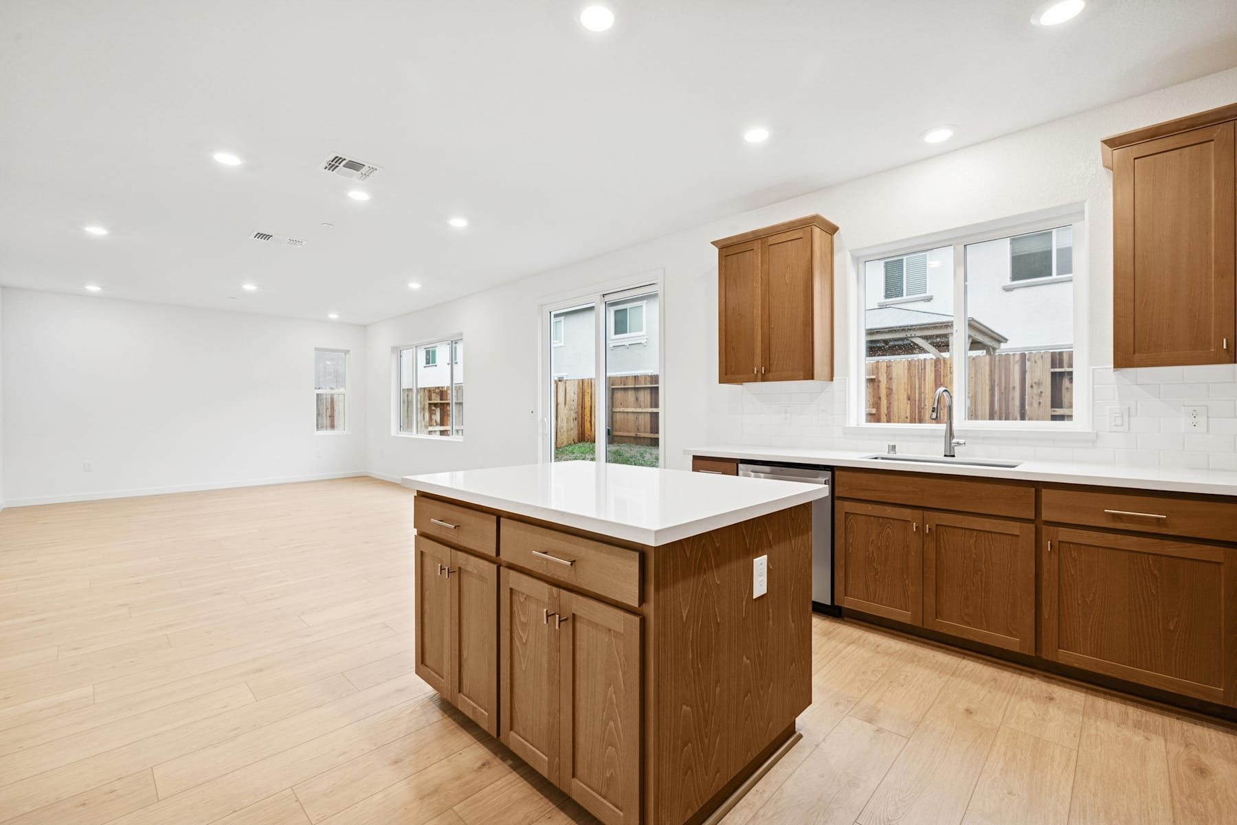 A spacious and modern kitchen with wooden cabinets, a white countertop, and a central island, set against a bright and airy background with large windows.