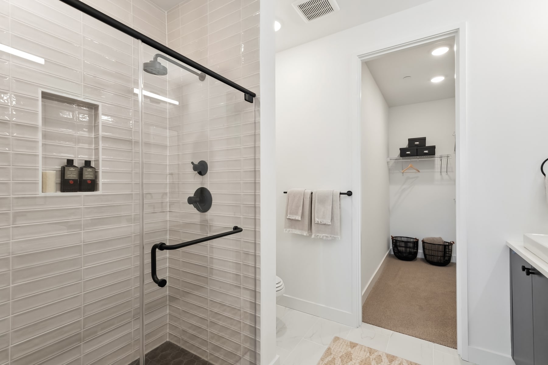 A modern, minimalist bathroom with a glass shower enclosure, white tile walls, and a mirror on the wall.