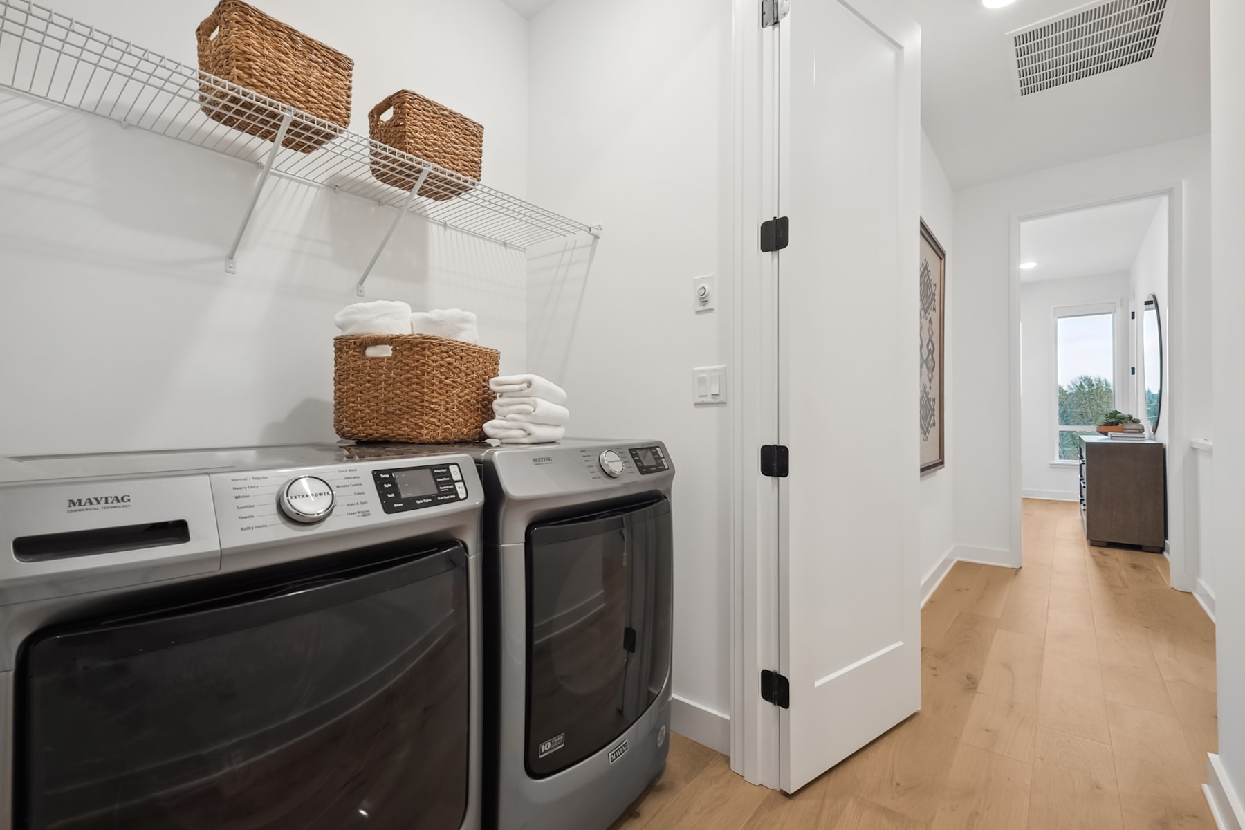A modern and minimalist laundry room with a washing machine and dryer, along with woven baskets for storage, set against a bright and airy backdrop.