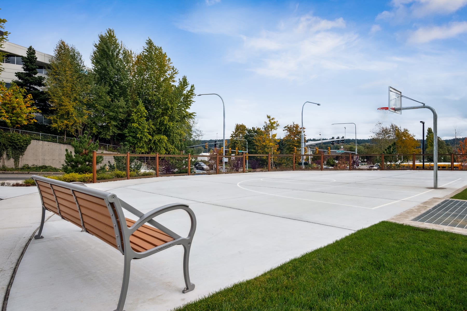 A paved basketball court surrounded by trees and benches, with a clear blue sky overhead.