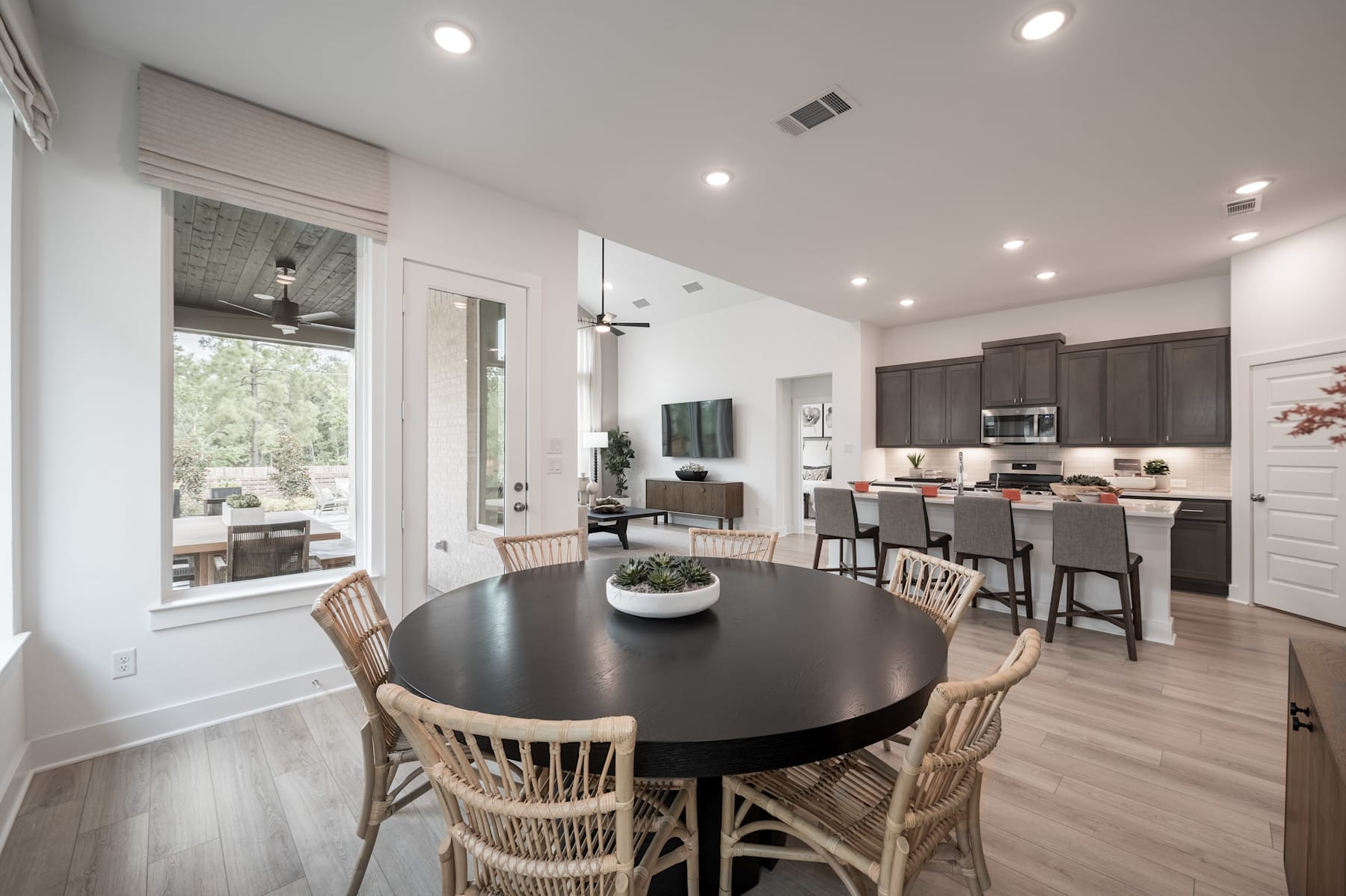 A modern and spacious open-plan kitchen and dining area with a large round dining table, wooden chairs, and a view of the living room in the background.