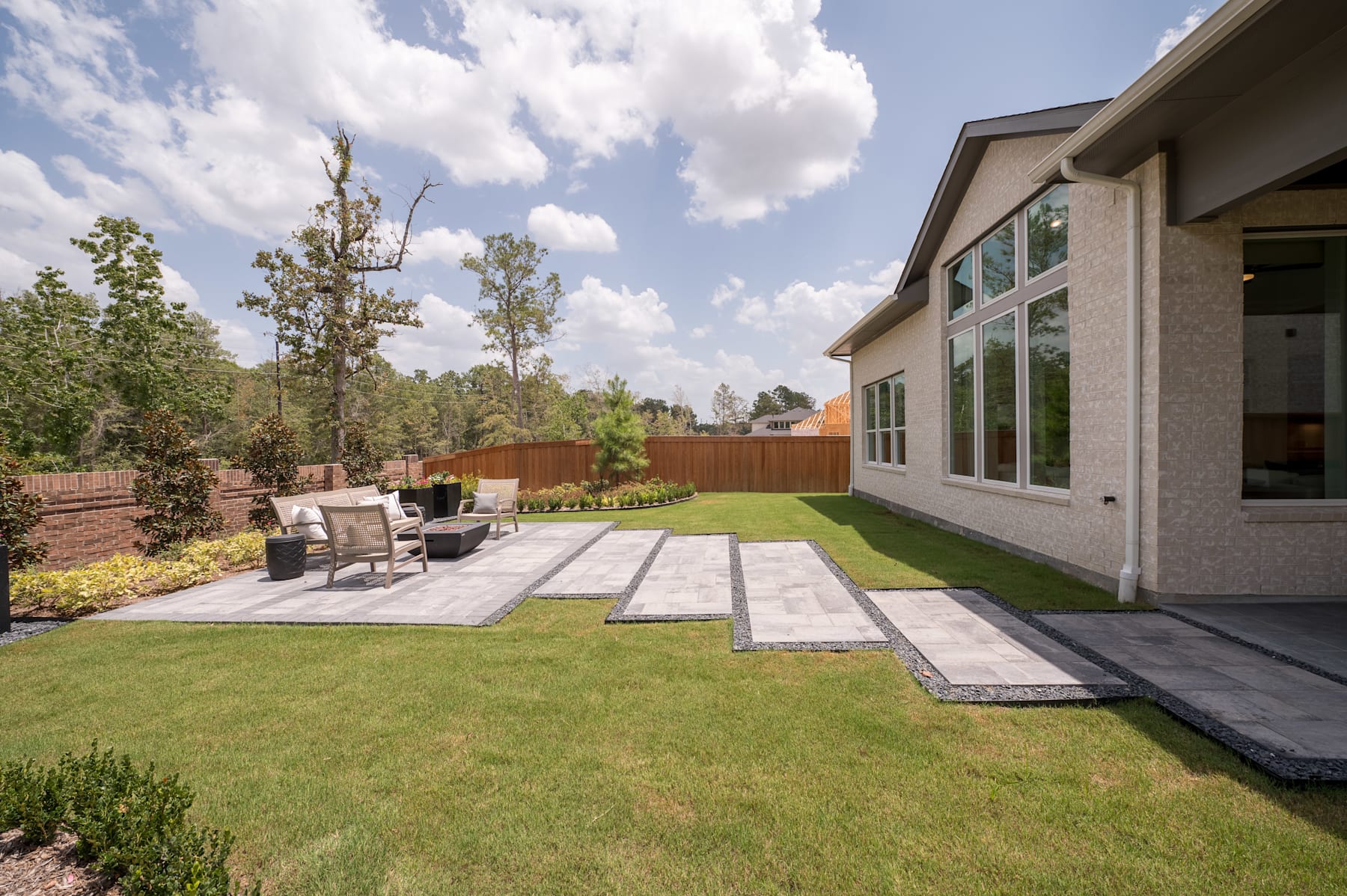 A well-manicured backyard with a paved patio, lush green lawn, and a modern house with large windows overlooking the scenic outdoor space.
