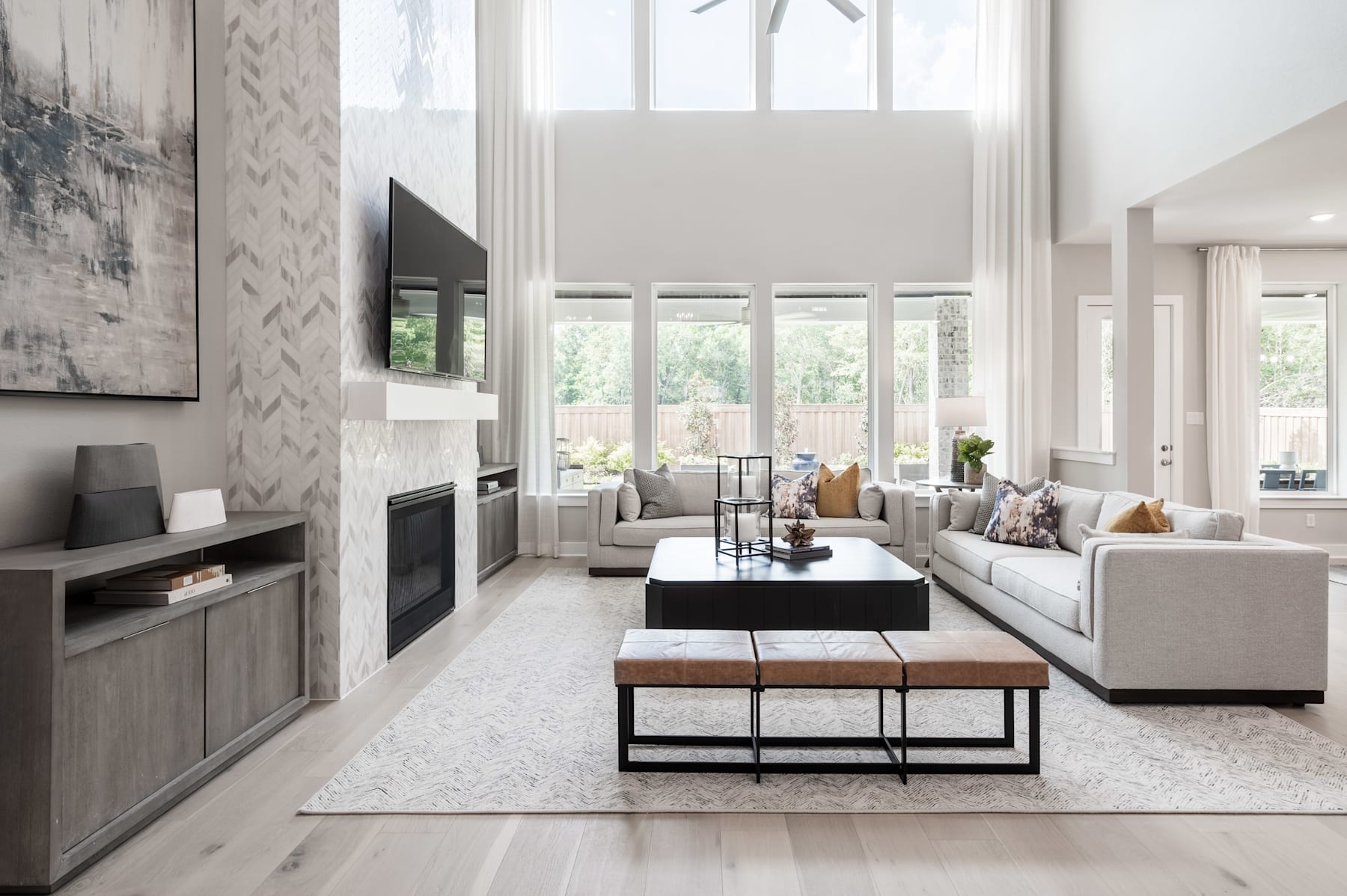 A modern and spacious living room with large windows, a fireplace, and a mix of neutral-toned furniture and decor.