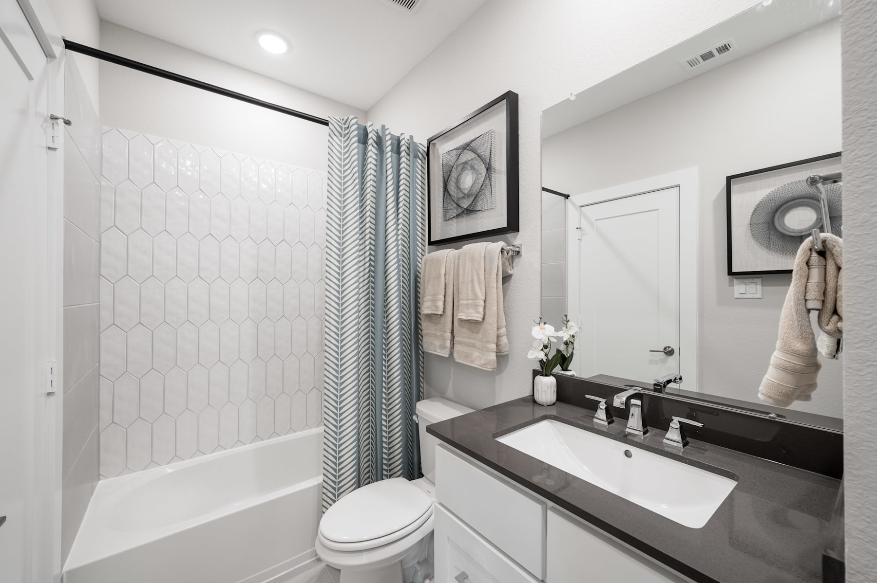 A modern and minimalist bathroom with a white vanity, a large mirror, and a patterned shower curtain, creating a clean and organized space.