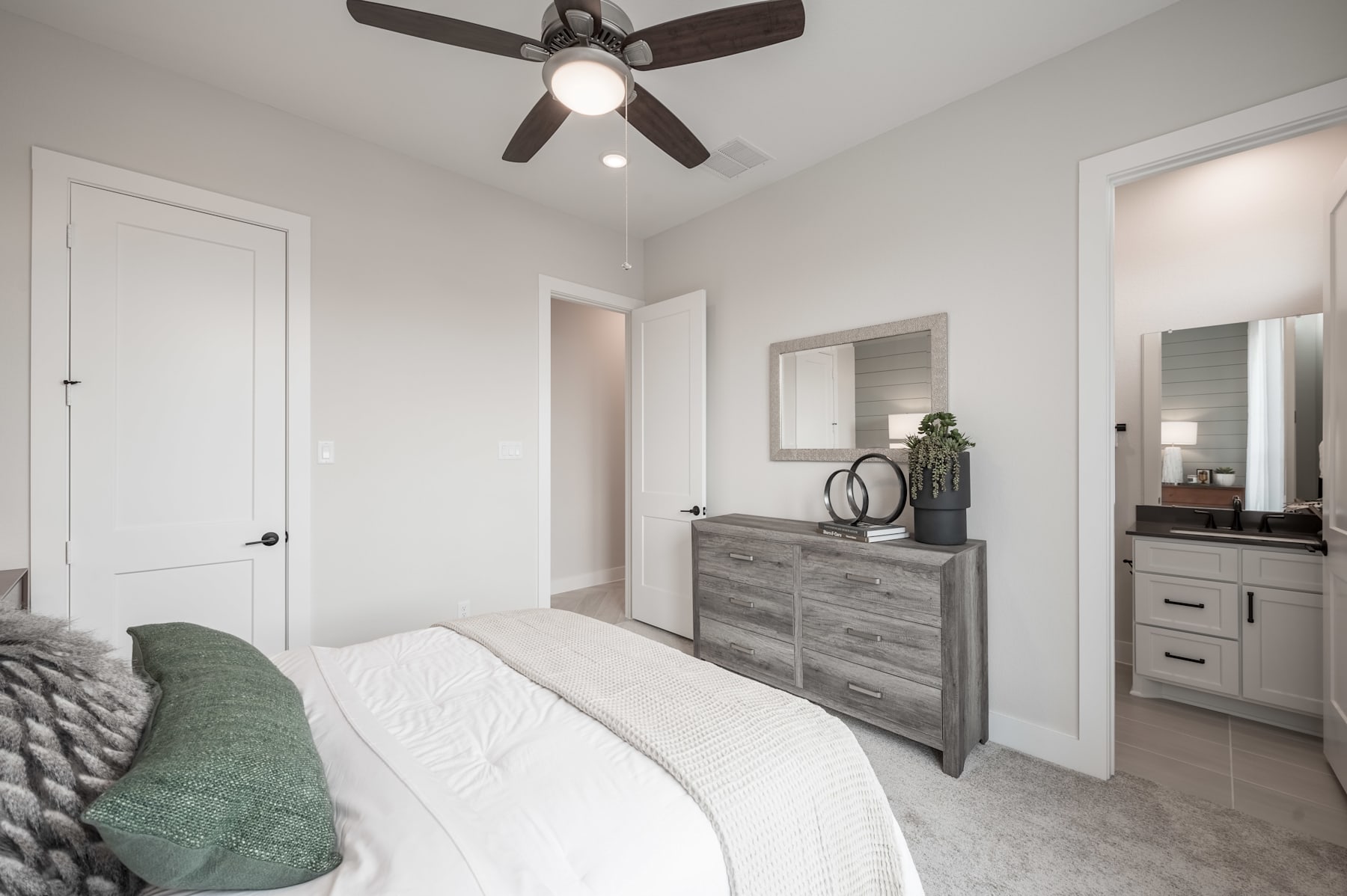 A cozy and modern bedroom with a ceiling fan, a dresser, and a mirror, set against a neutral color palette and clean lines.
