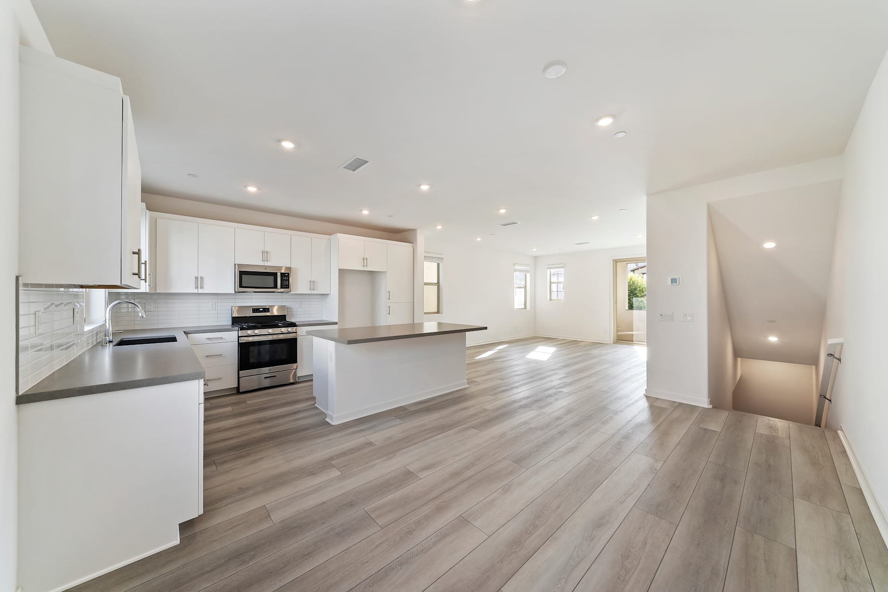 A modern, open-concept kitchen and living space with white cabinets, stainless steel appliances, and a hardwood floor that extends throughout the room.