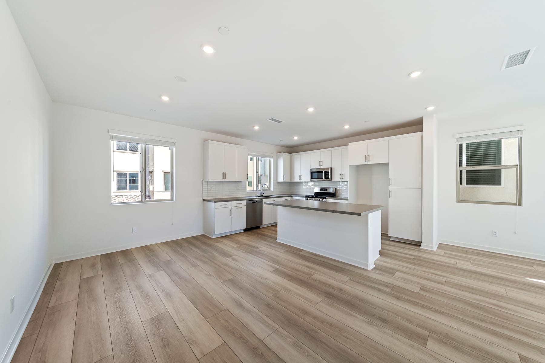A modern, open-concept kitchen with white cabinets, stainless steel appliances, and a hardwood floor that extends throughout the room.