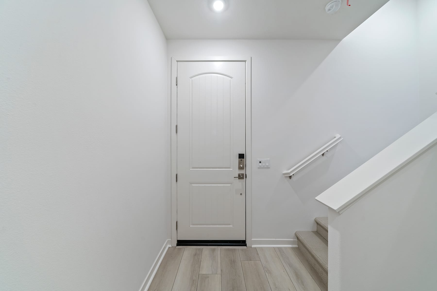 A white door stands in a bright, minimalist hallway with light-colored wood flooring.