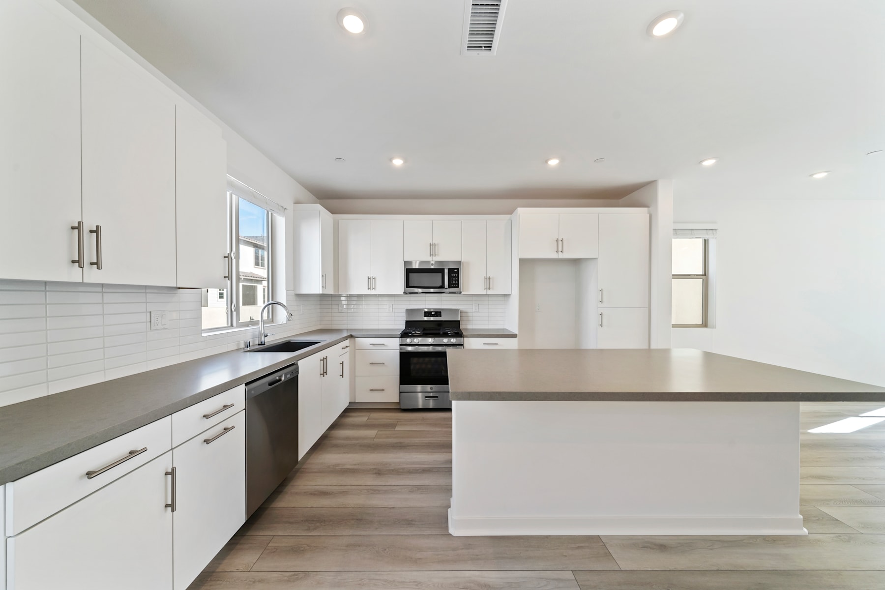 A modern, bright, and spacious kitchen with white cabinets, stainless steel appliances, and a large central island with a countertop.