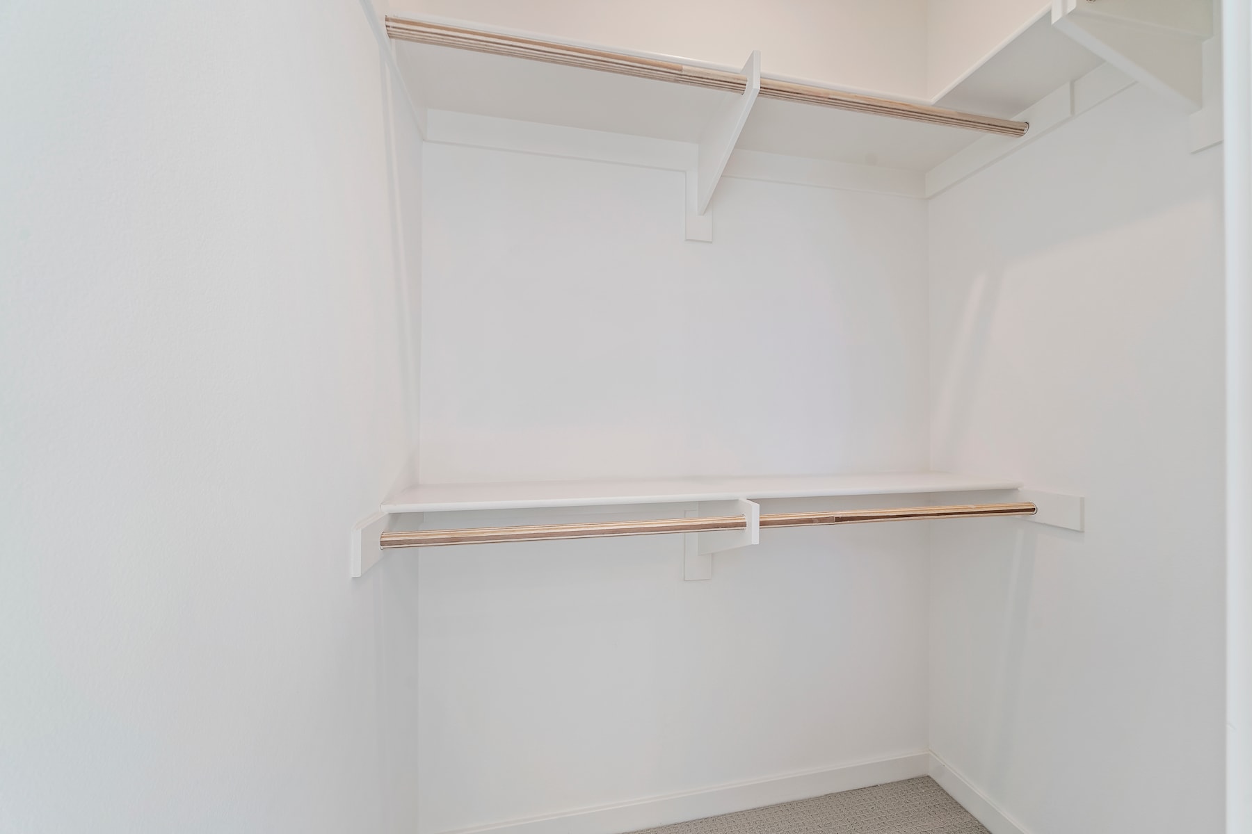 A simple, minimalist closet space with white walls and wooden shelves.