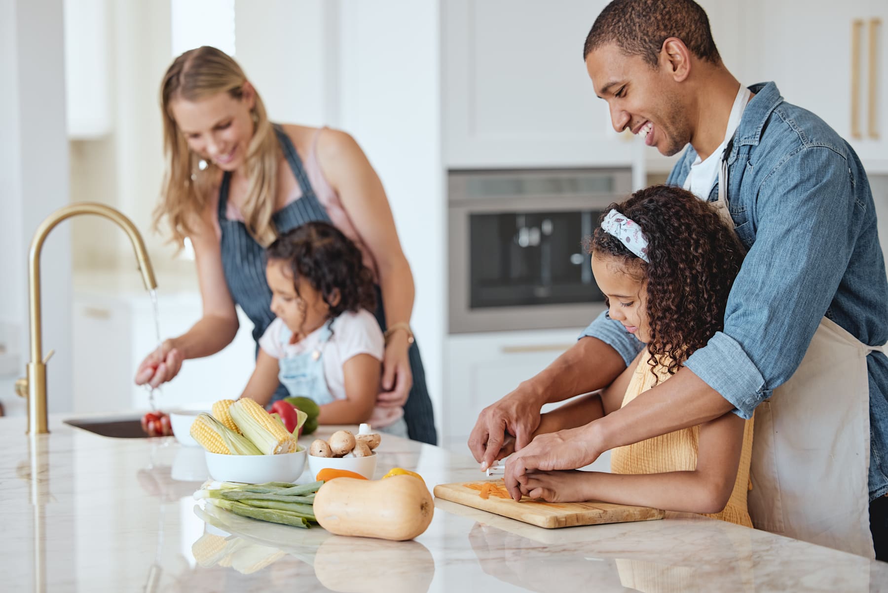 A family of four is gathered in the kitchen, preparing food together on the countertop.
