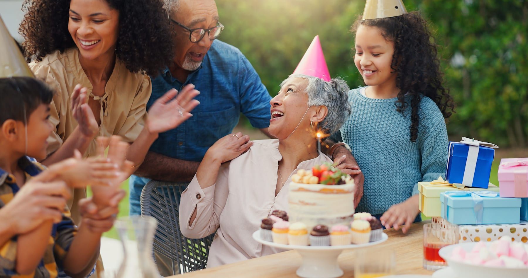 A multigenerational family celebrating a birthday together outdoors, with a cake, gifts, and a joyful atmosphere.