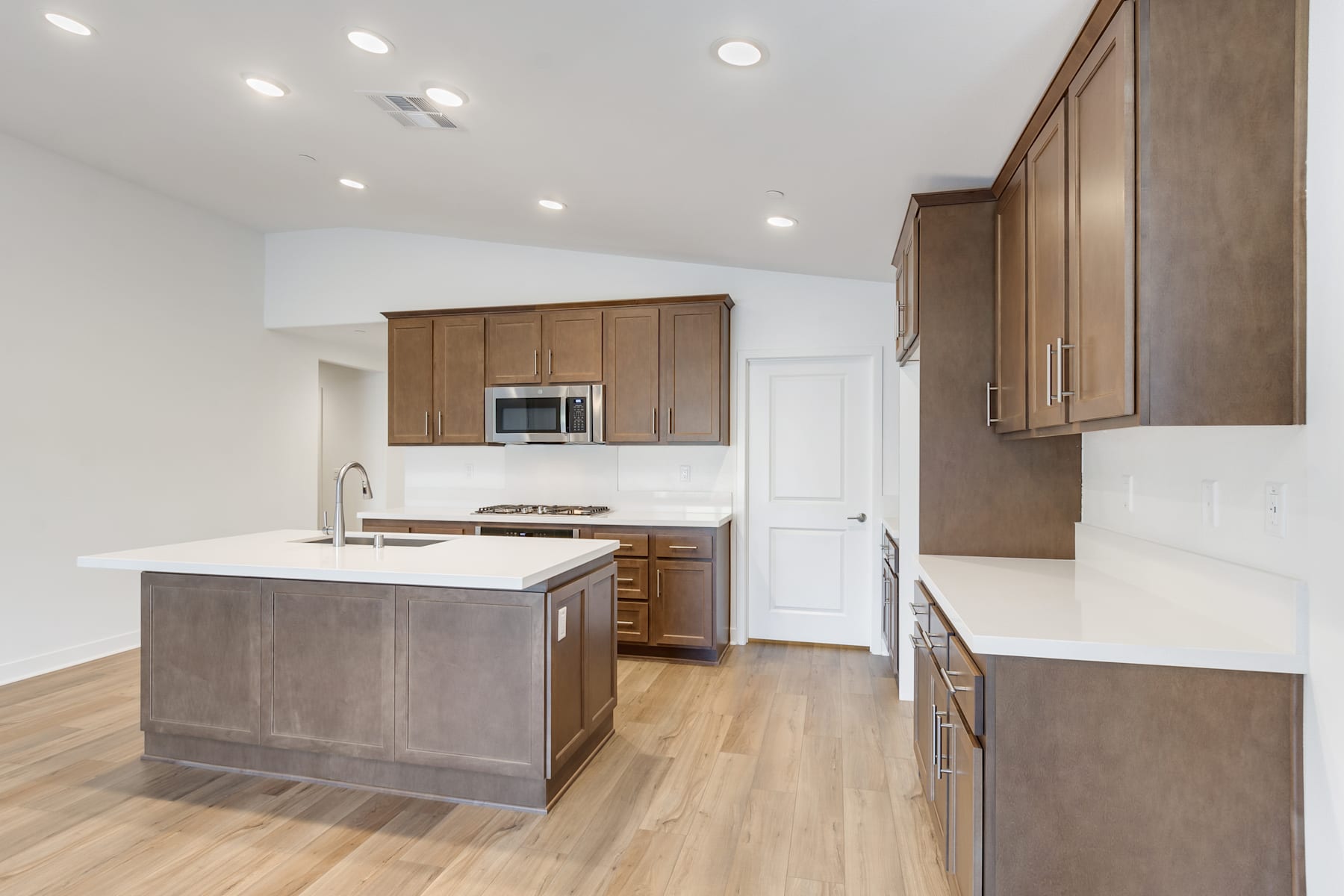 A modern, open-concept kitchen with light wood cabinets, a central island, and hardwood flooring.