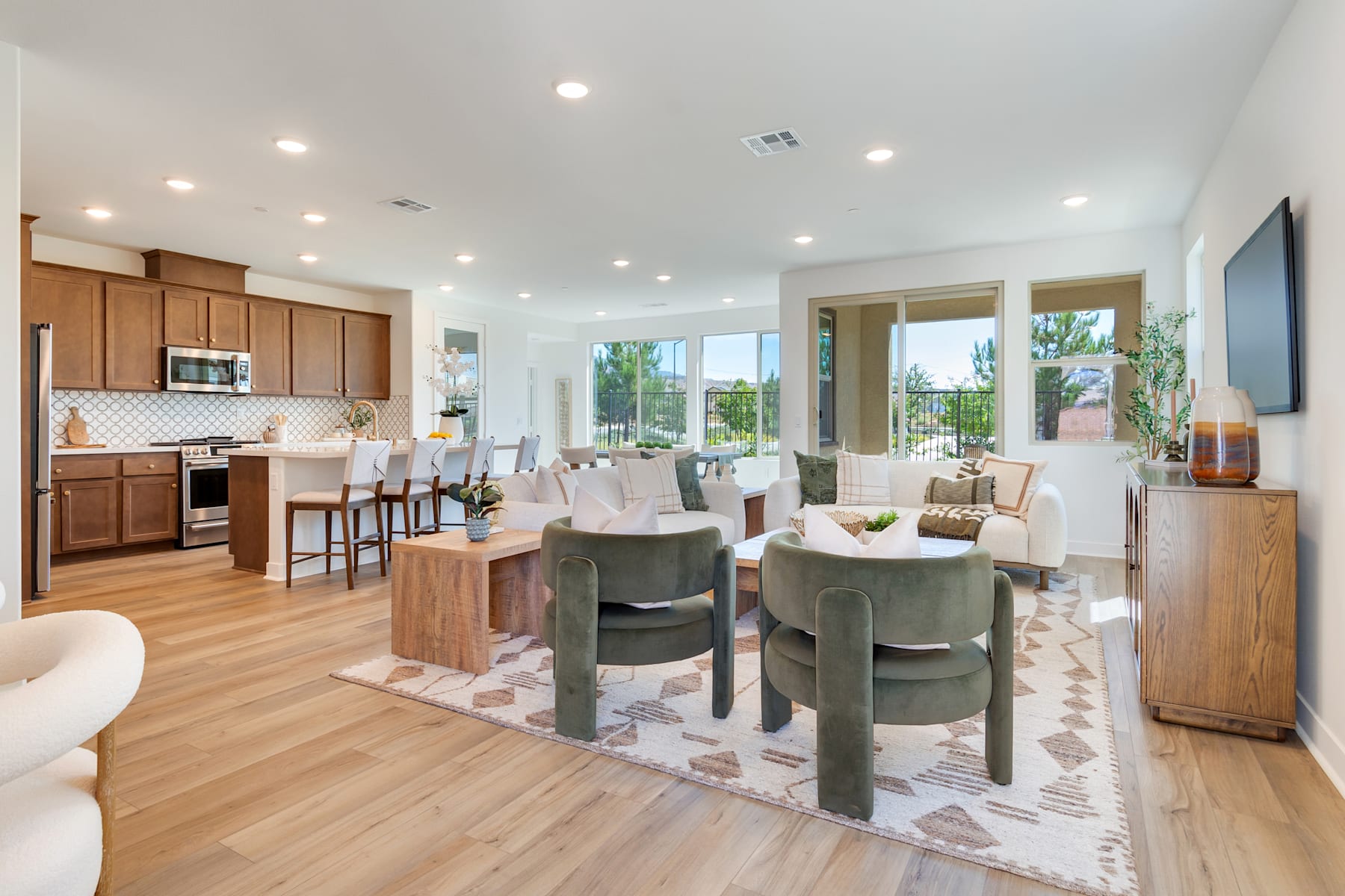 A spacious and modern open-plan living area with a kitchen, dining, and living room, featuring wooden furniture, plush seating, and large windows overlooking a scenic outdoor view.