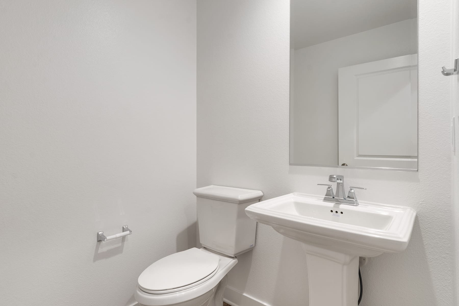 A simple and clean bathroom with a white toilet, sink, and mirror against a plain white wall.