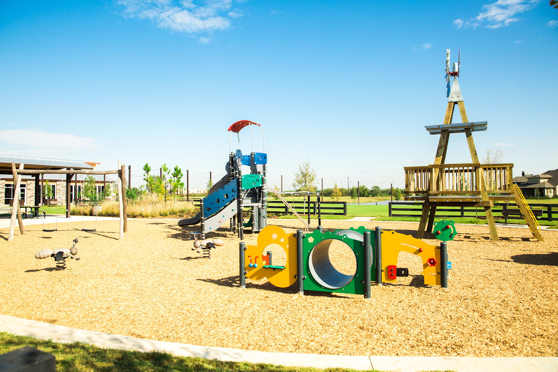 A colorful playground with various play structures, including a slide and climbing equipment, set against a backdrop of a clear blue sky and lush greenery.