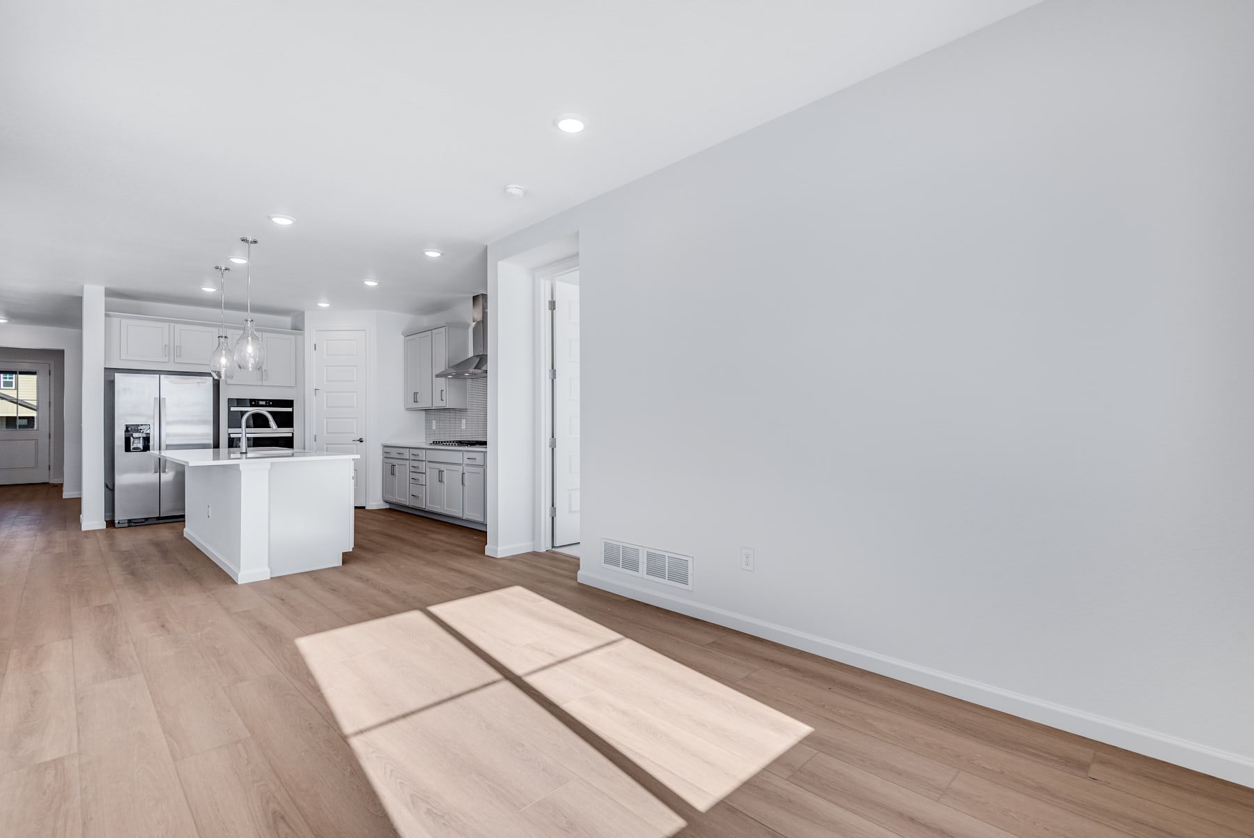 A modern, open-concept kitchen with white cabinets, hardwood floors, and recessed lighting, leading into a bright and airy living space.