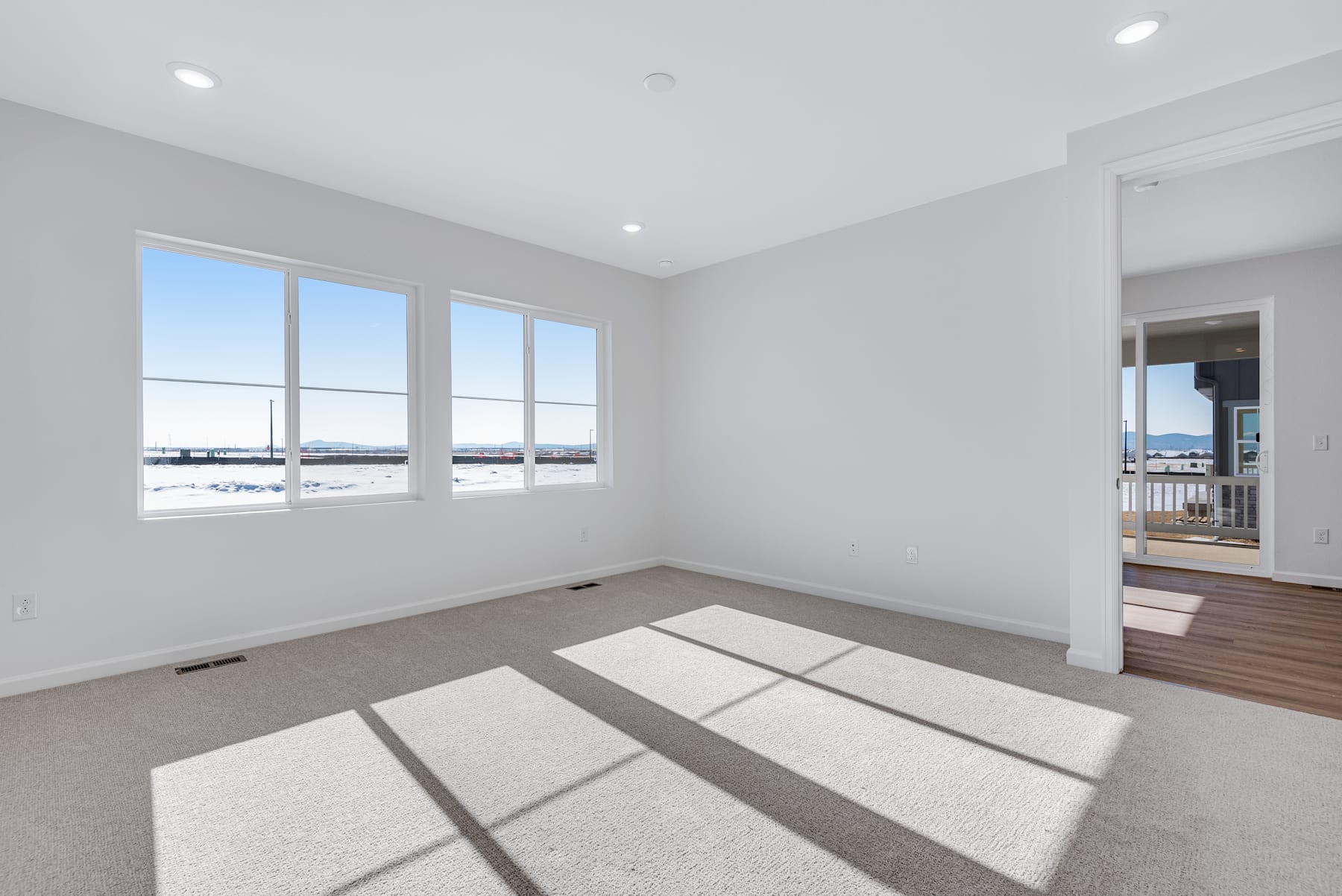 A spacious, bright room with large windows overlooking a scenic outdoor view, featuring a hardwood floor and a neutral color scheme.