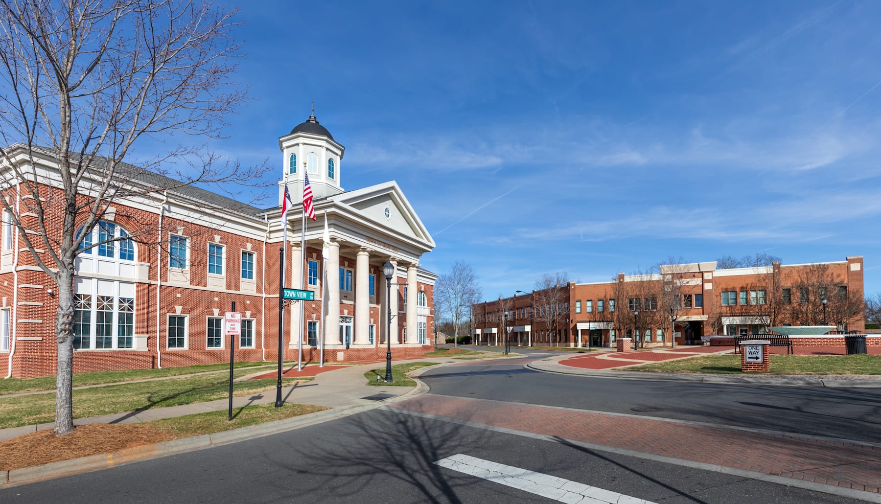 A brick building with a clock tower stands prominently in the foreground, surrounded by trees and a paved walkway leading to other buildings in the background.