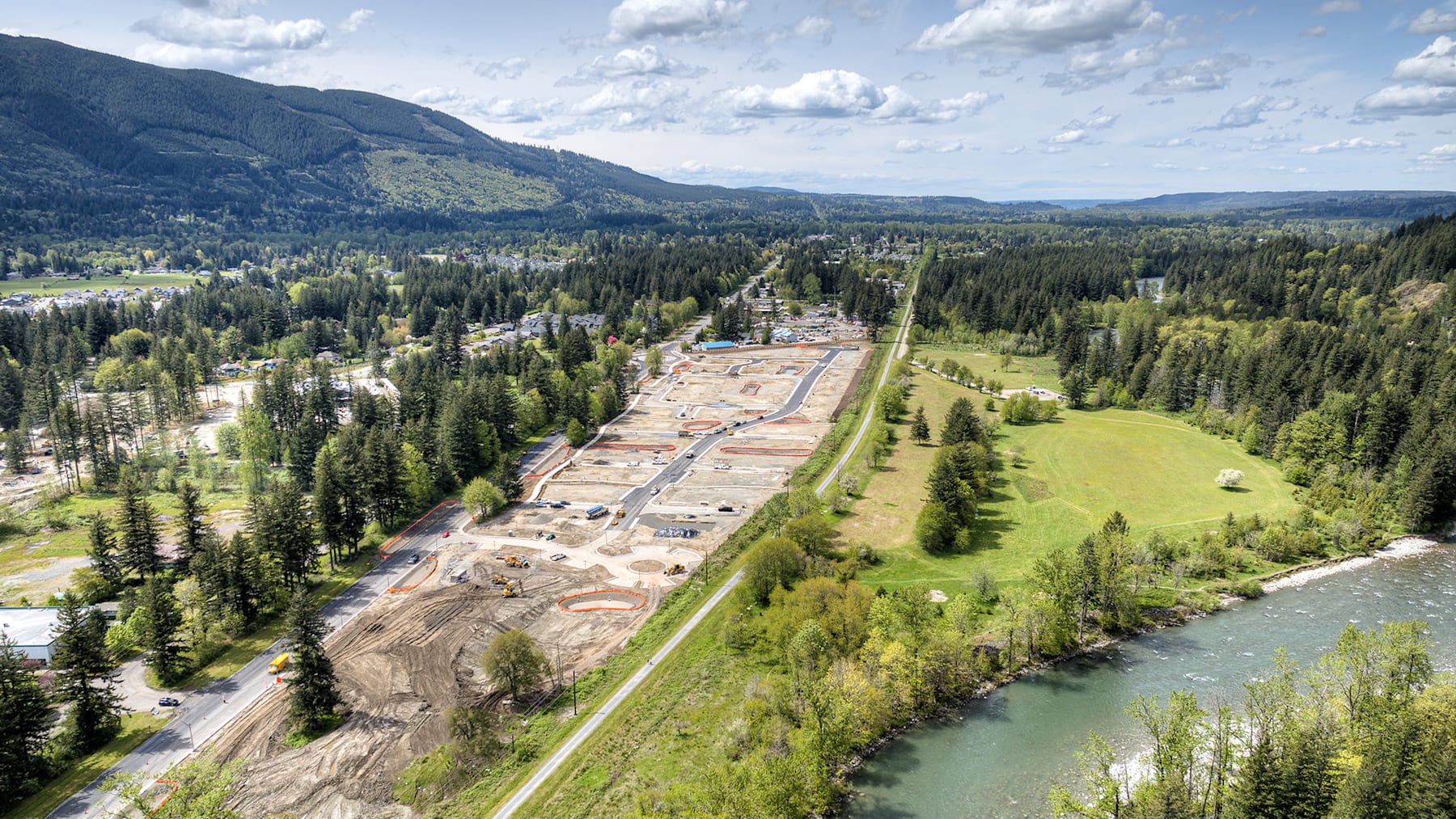 A lush, forested landscape with a winding river and a small town nestled in the valley, surrounded by towering mountains under a cloudy sky.