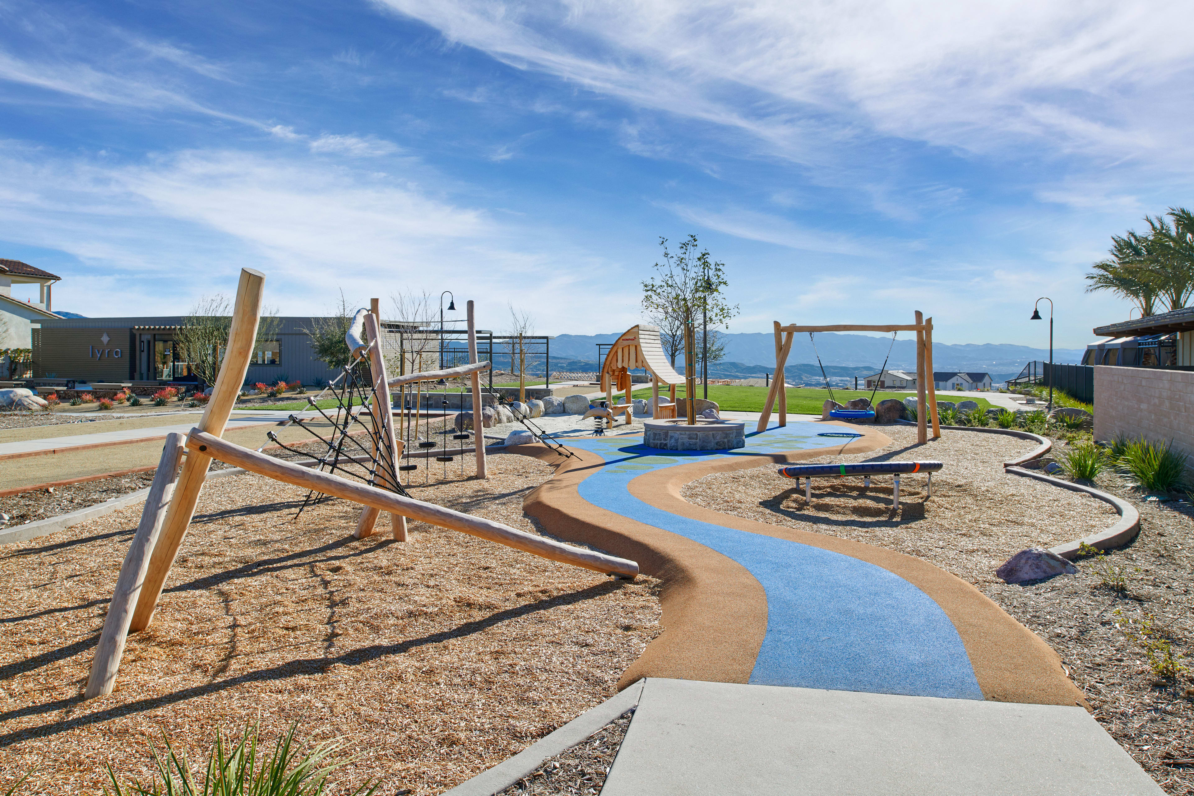A colorful and vibrant outdoor playground with various play structures, a winding path, and a scenic backdrop of a blue sky with wispy clouds.