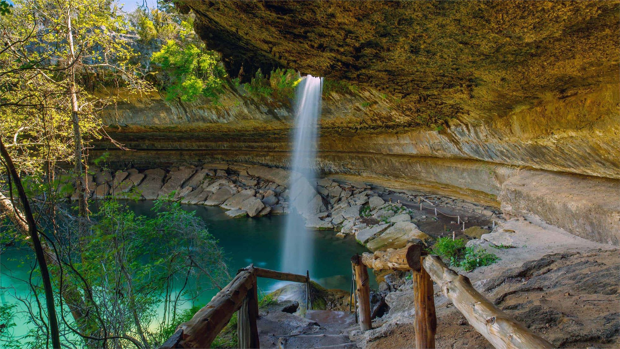 A stunning waterfall cascades down a rocky cliff, surrounded by lush greenery and a tranquil turquoise pool in the foreground.