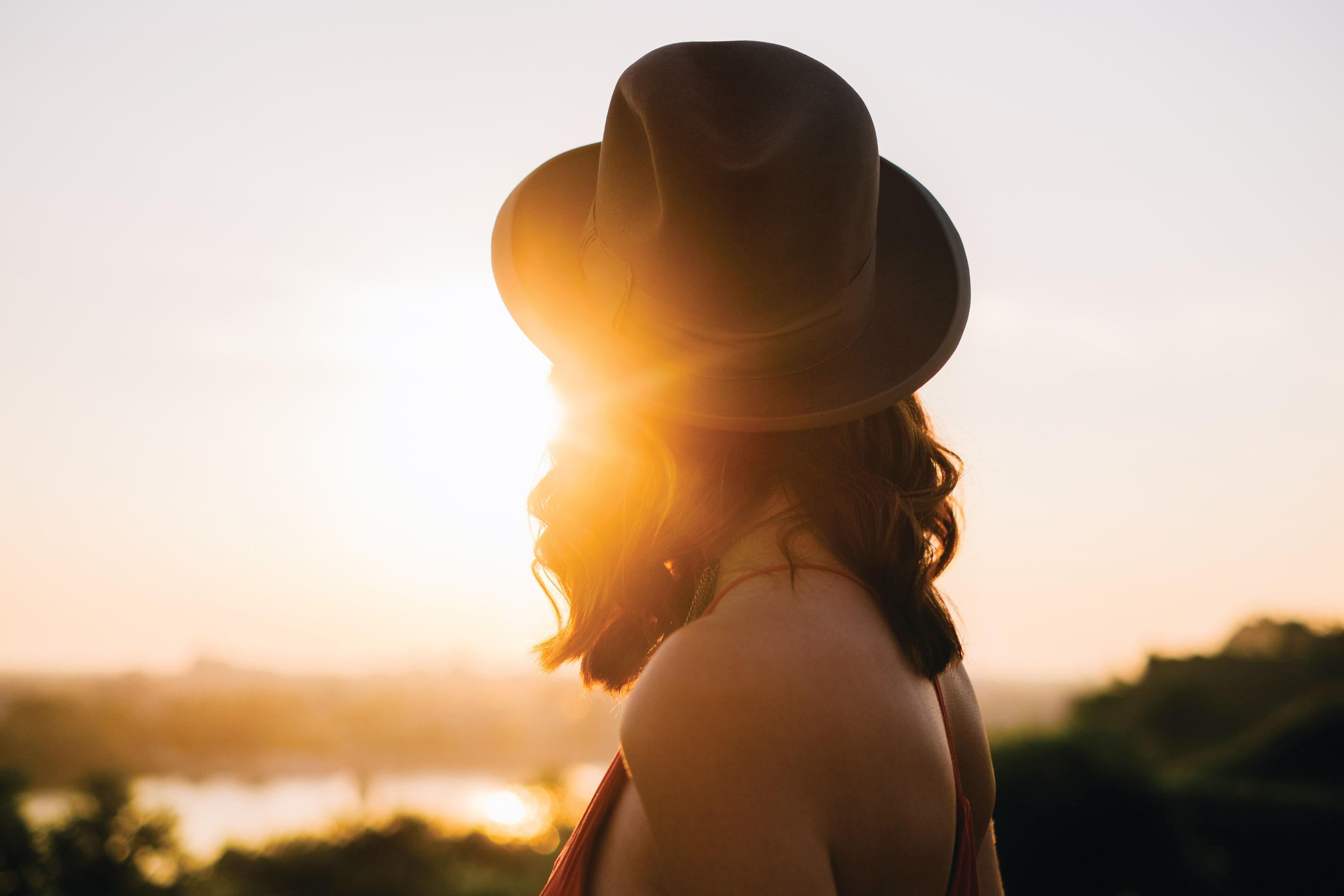 A silhouetted figure stands against a vibrant sunset, with the warm glow of the sun casting a soft light on the surroundings.