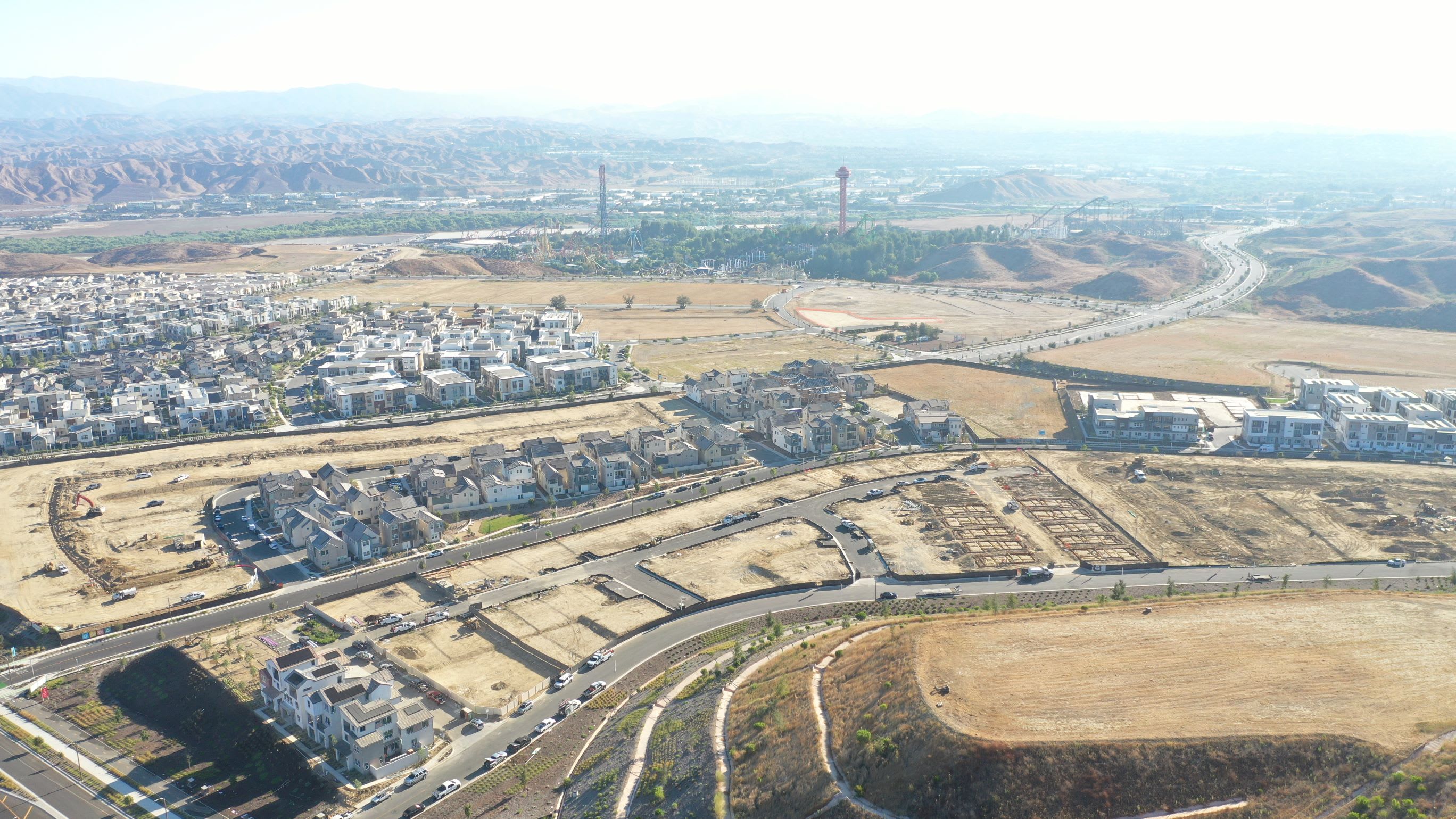 A sprawling urban landscape with a mix of residential and industrial areas, surrounded by rugged terrain and hazy mountains in the distance.