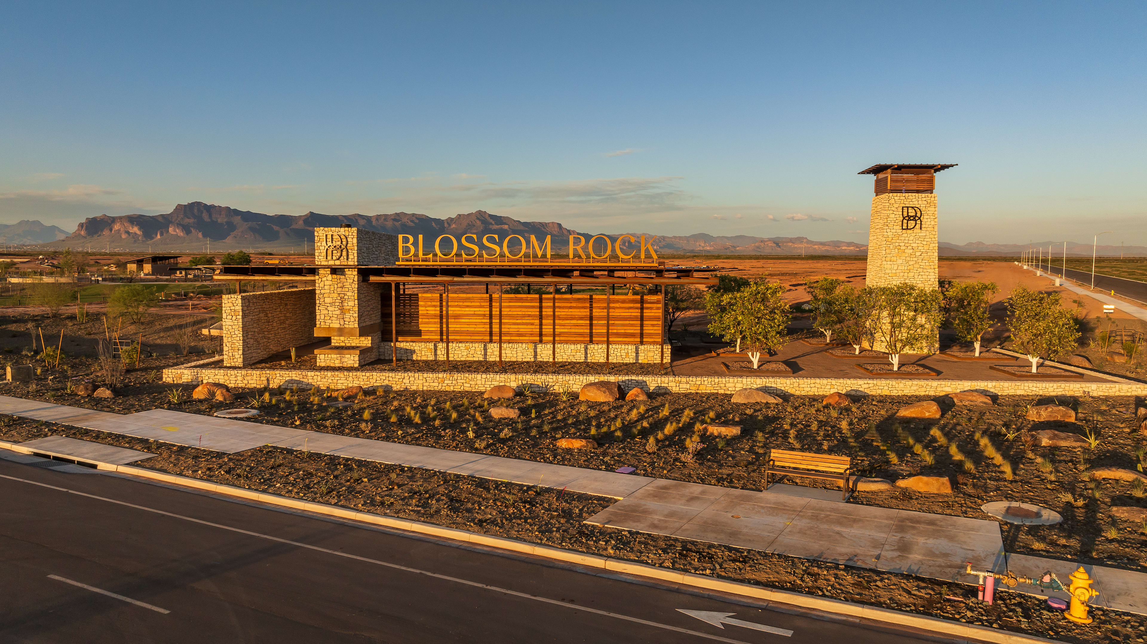 A large, modern building with the name "Blossom Rock" prominently displayed stands in the foreground, surrounded by a rocky landscape and mountains in the background under a clear blue sky.