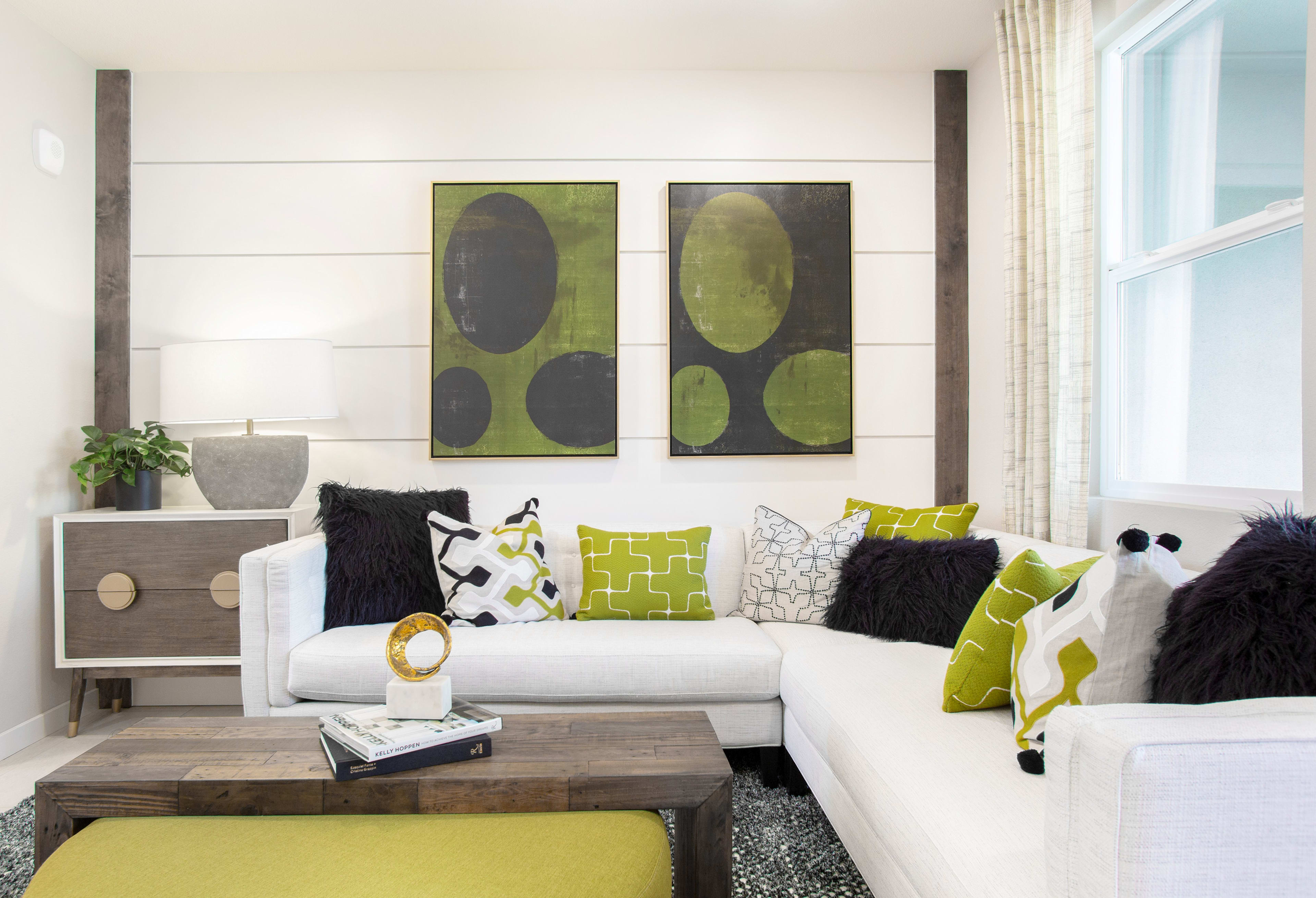 A modern and stylish living room with a white sofa, patterned throw pillows, and abstract artwork on the walls, set against a backdrop of shiplap paneling and a large window.
