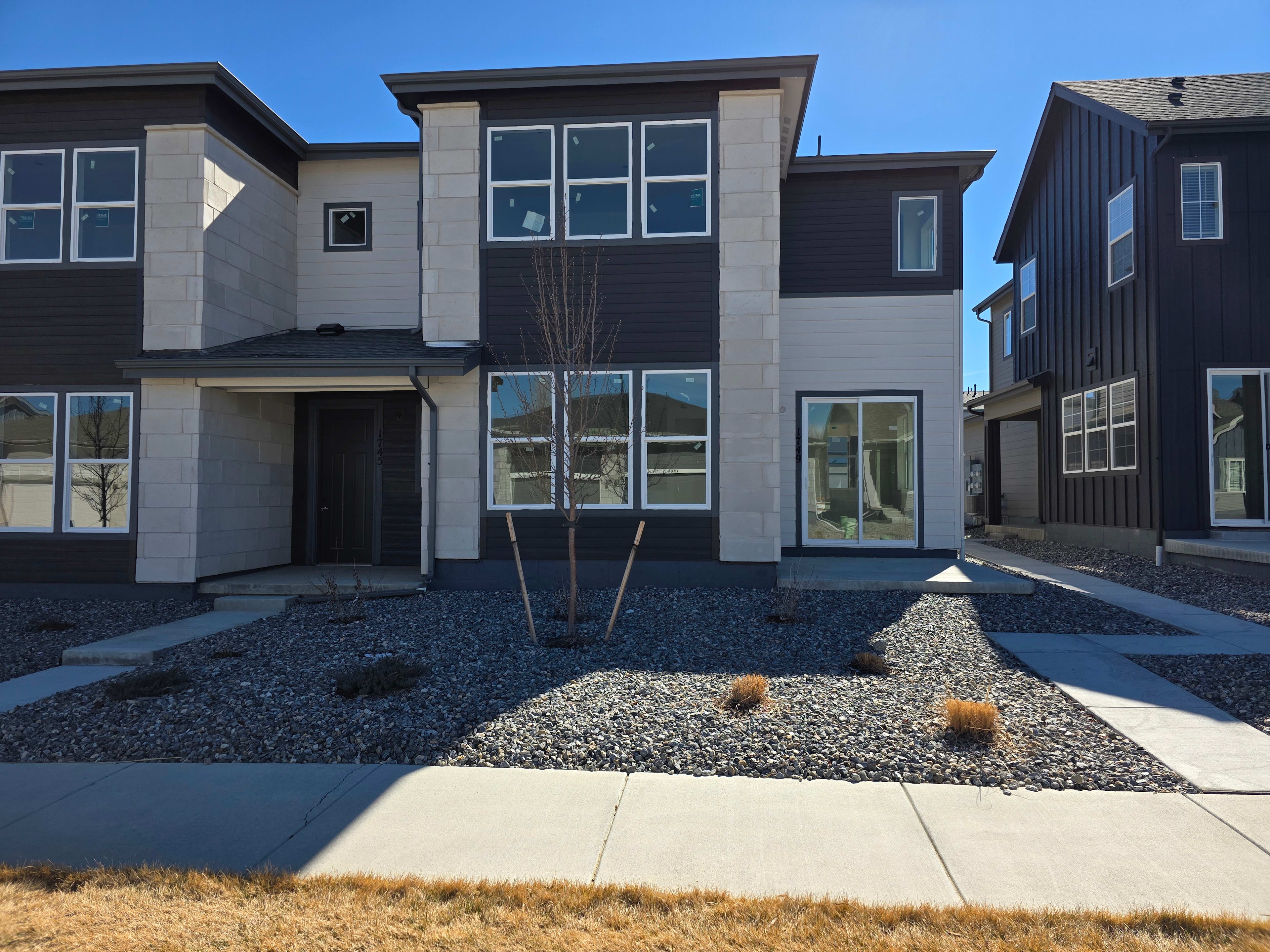 A modern multi-story residential building with a paved walkway, gravel landscaping, and a clear blue sky in the background.