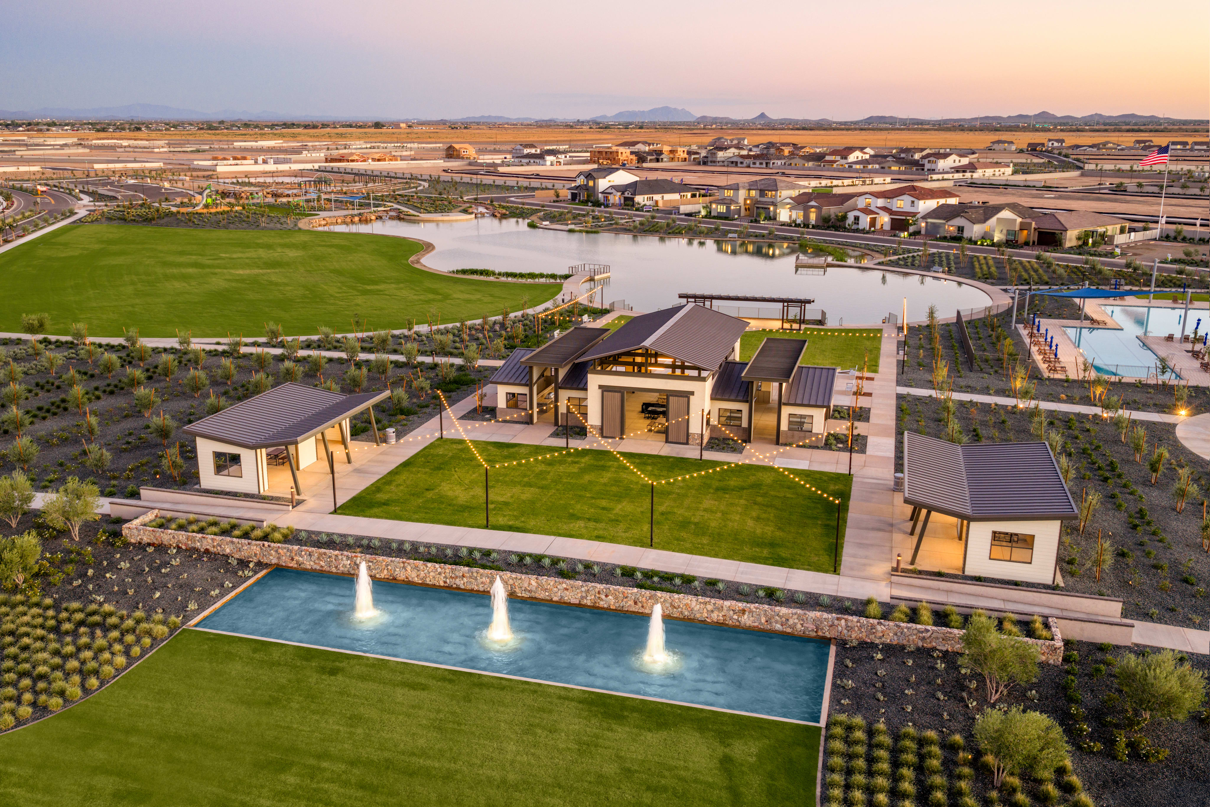 A residential community with a central pool and landscaped grounds, surrounded by a vast expanse of desert landscape and mountains in the distance.